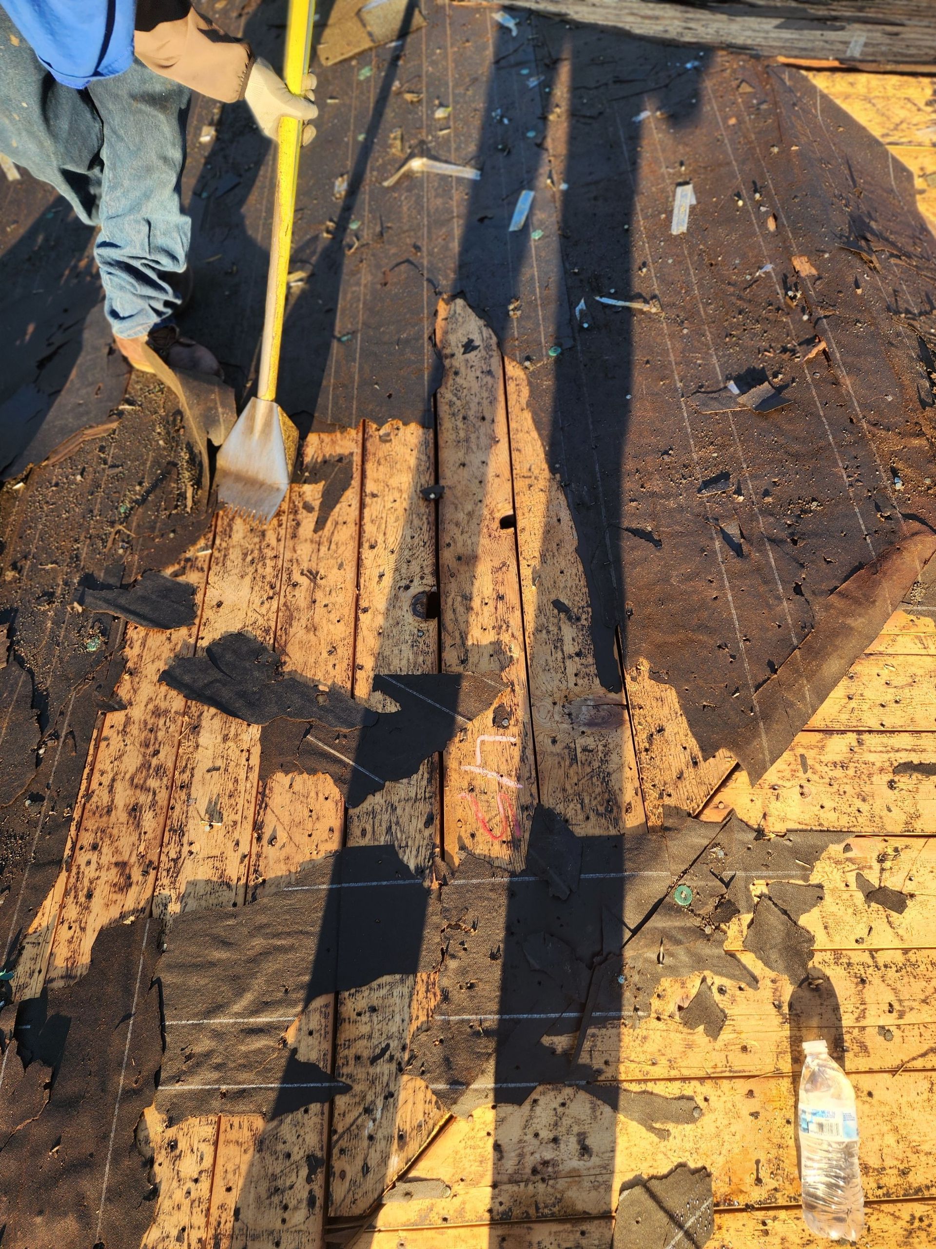Worker using a shovel on a muddy rooftop or deck with boards and scattered debris.