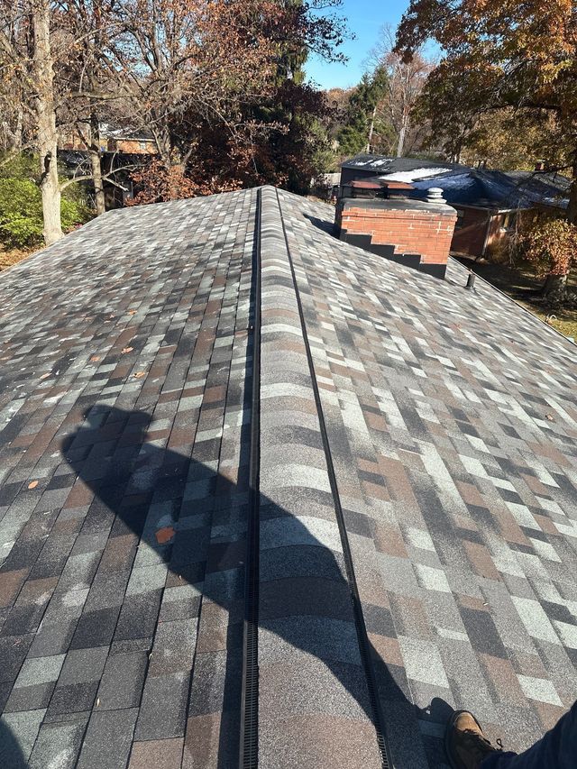 Roof covered with gray shingles, viewed from the ridge in daylight.