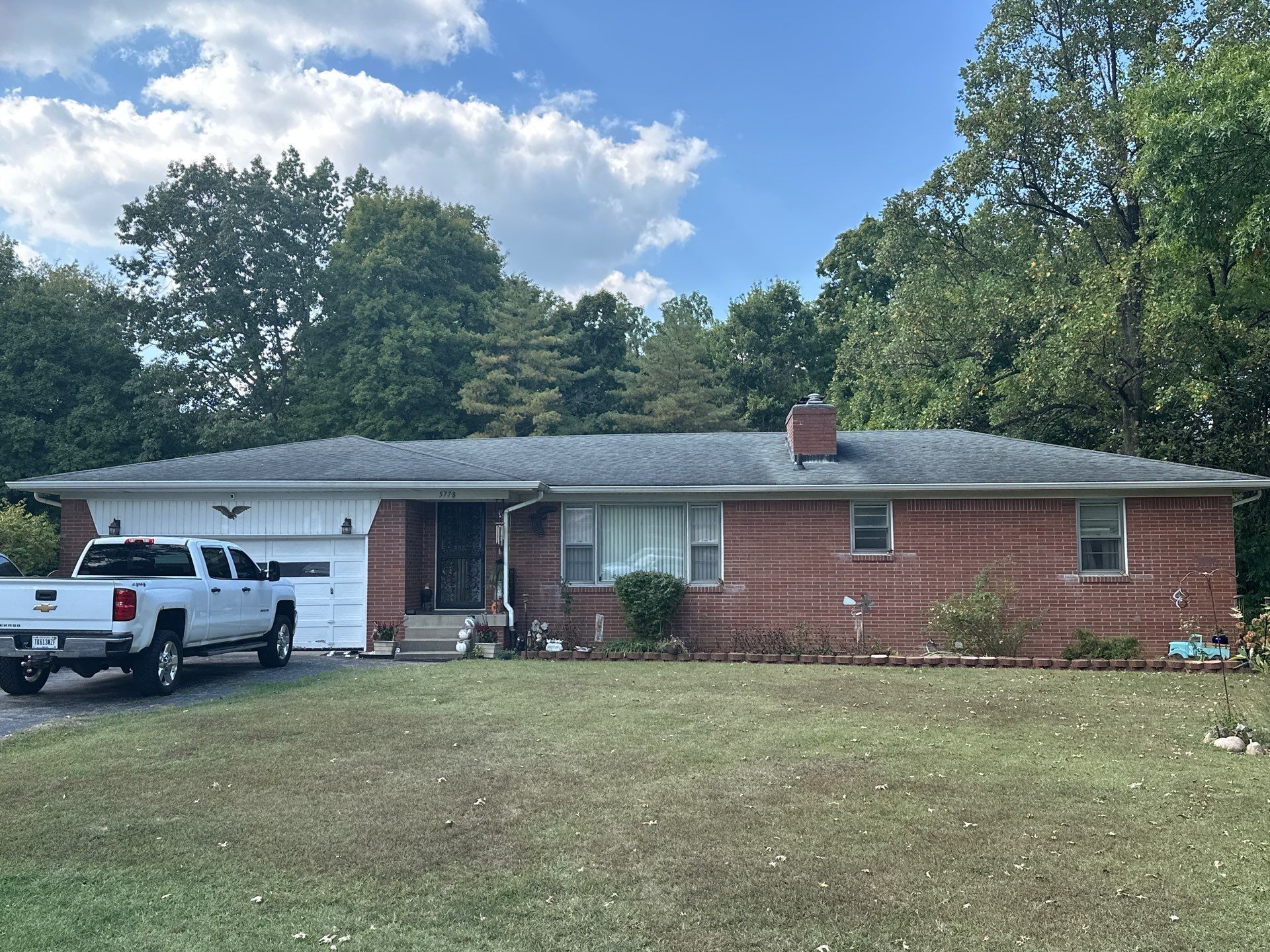 Single-story brick house with white garage, parked pickup truck, and large front lawn under a blue sky