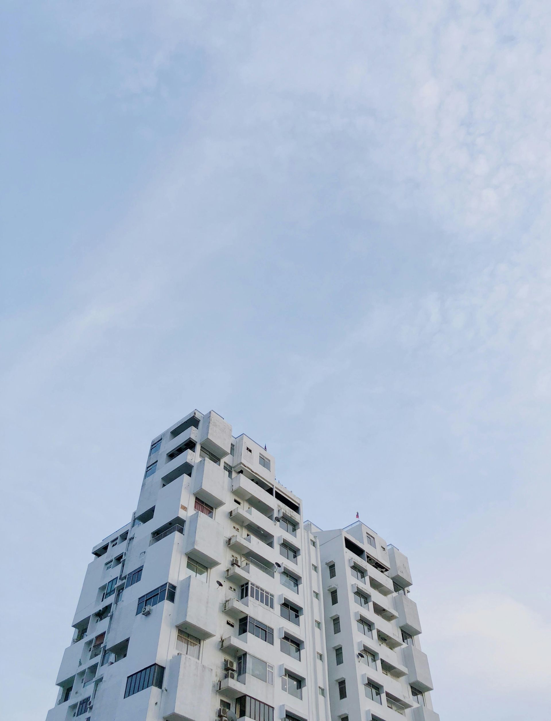 Tall white apartment building against a pale blue sky