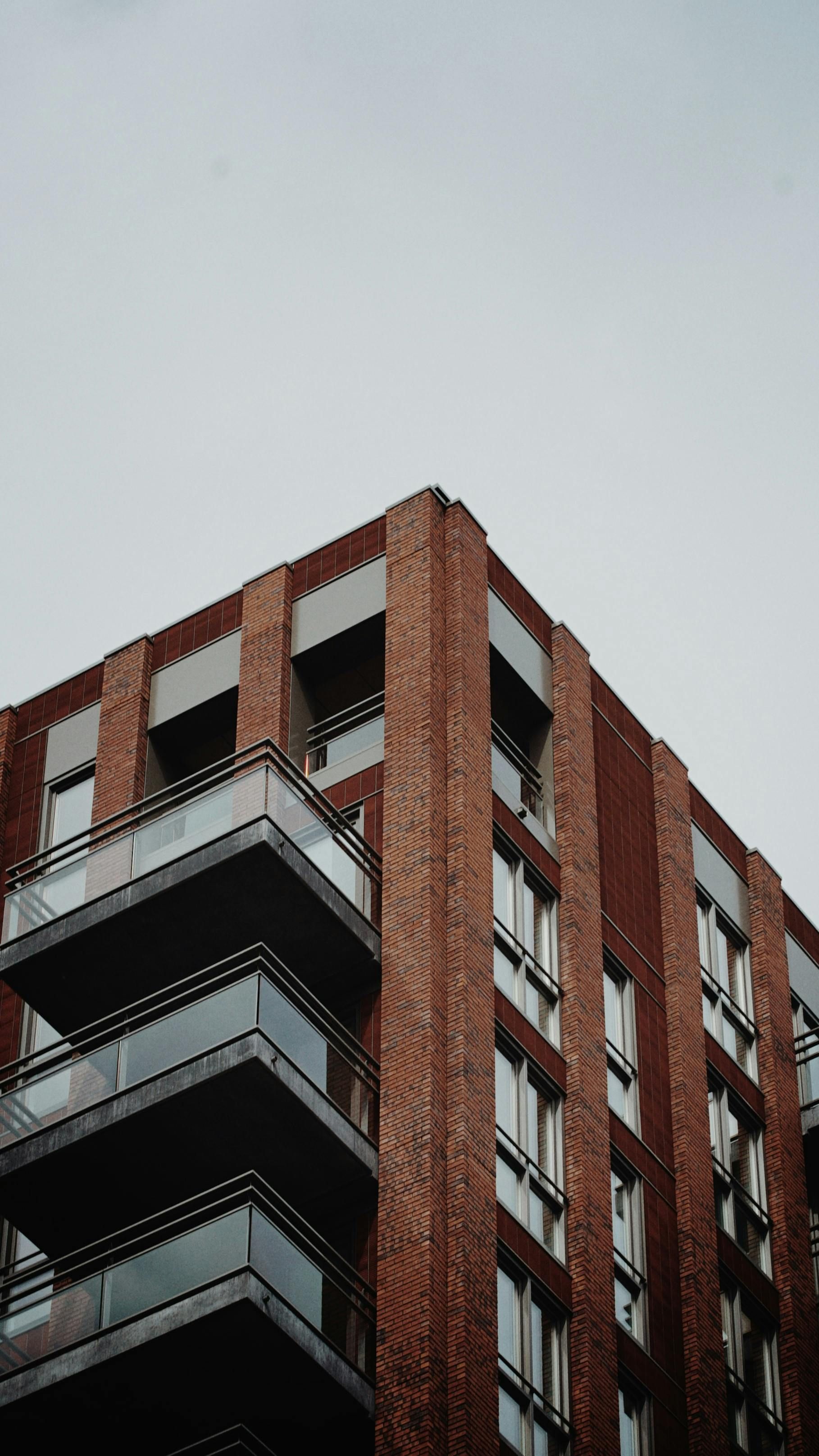 Tall brick apartment building with dark balconies against a gray sky