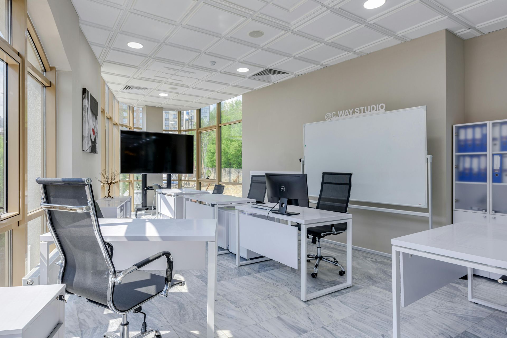 Modern office with desks, chairs, computer monitors, and a large whiteboard in a bright room