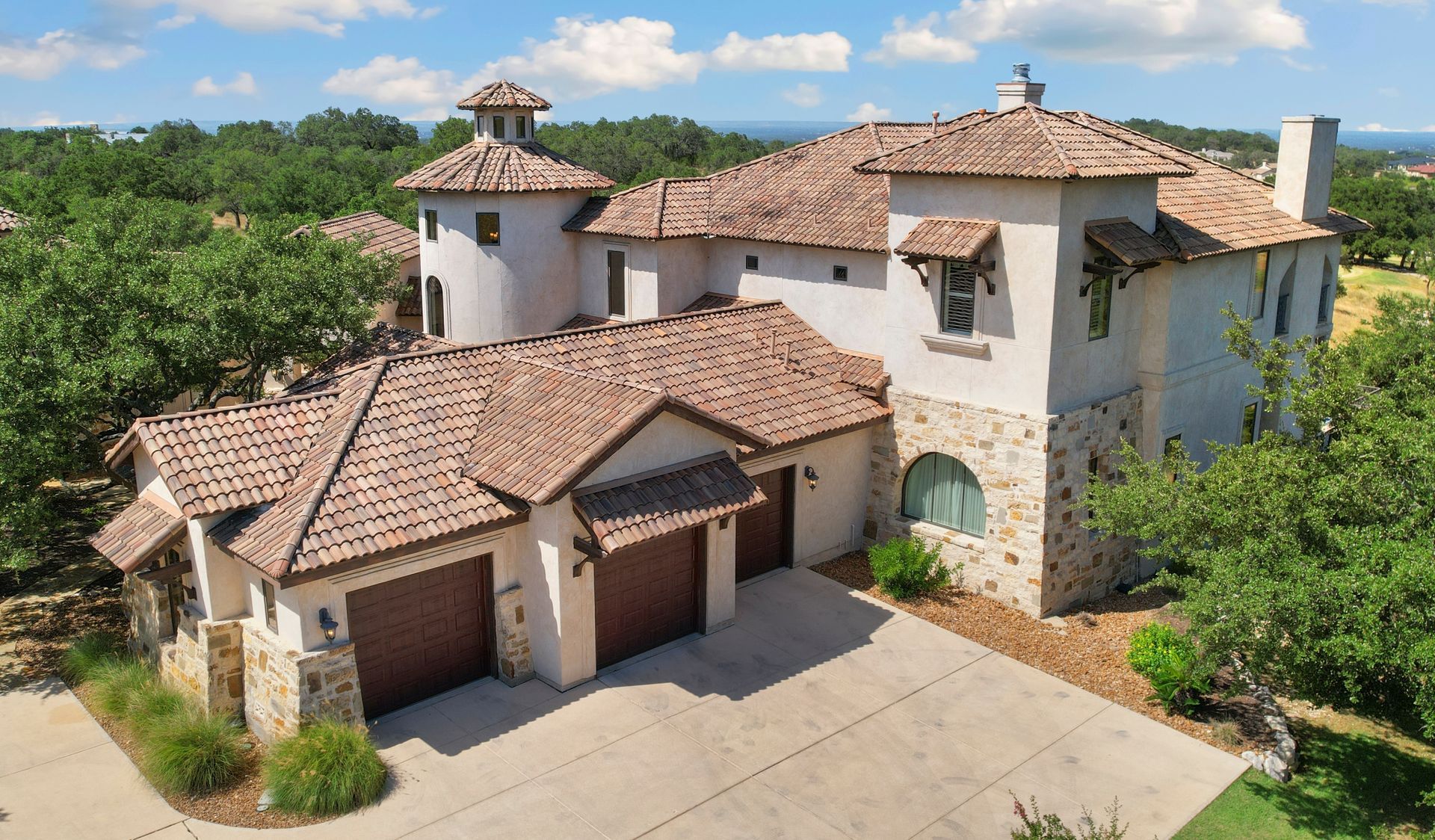 Large Mediterranean-style house with red-tiled roofs, stucco walls, and a spacious driveway