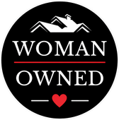 Black circular badge reading “WOMAN OWNED” with a red heart and white house graphic.