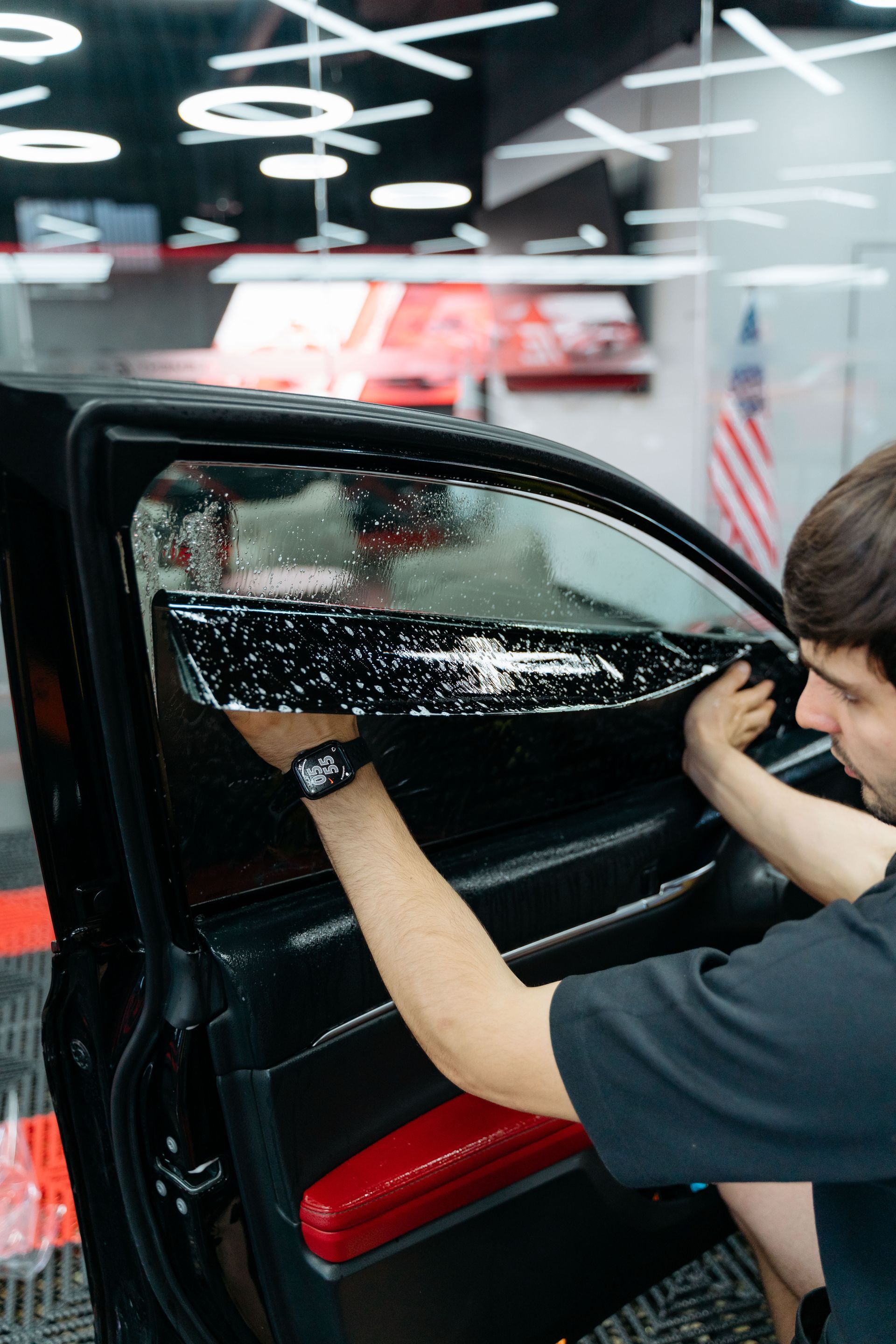 Person tinting a car window with a squeegee in a garage