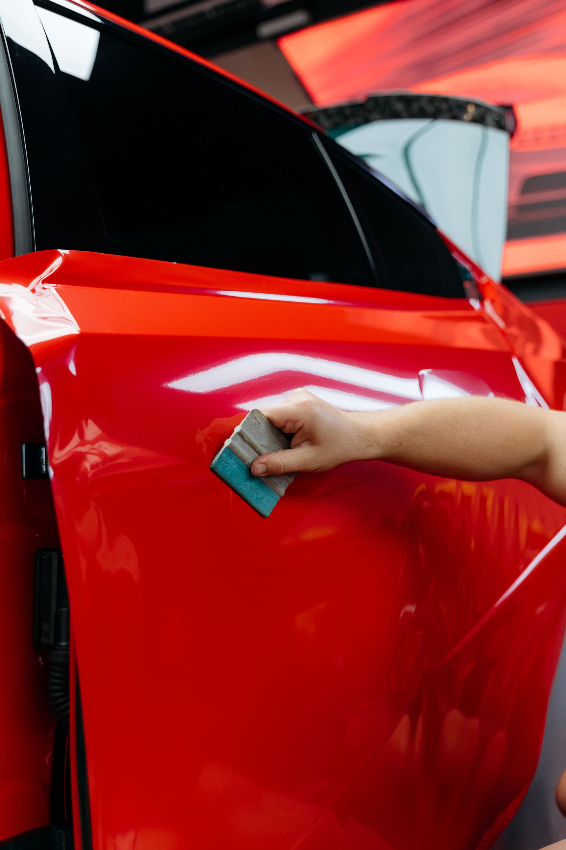 Hand cleaning a shiny red car door with a sponge near an open window