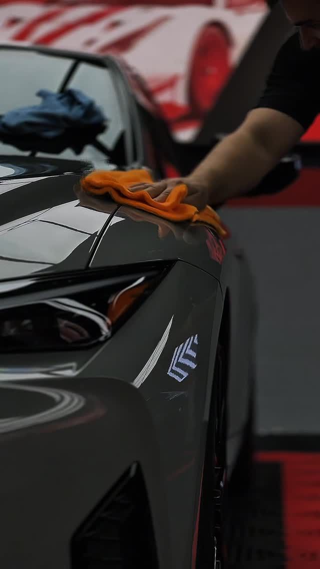 Hand polishing a black sports car hood with an orange cloth at an auto show