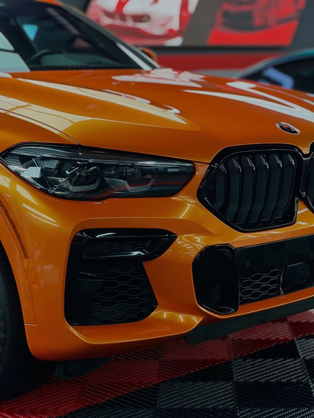 Orange BMW sports car front close-up on a checkered floor, with black grille and headlights.