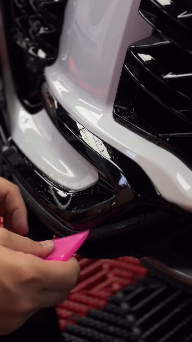 Hand holding a pink tool near a white car bumper, inspecting a damaged grille area