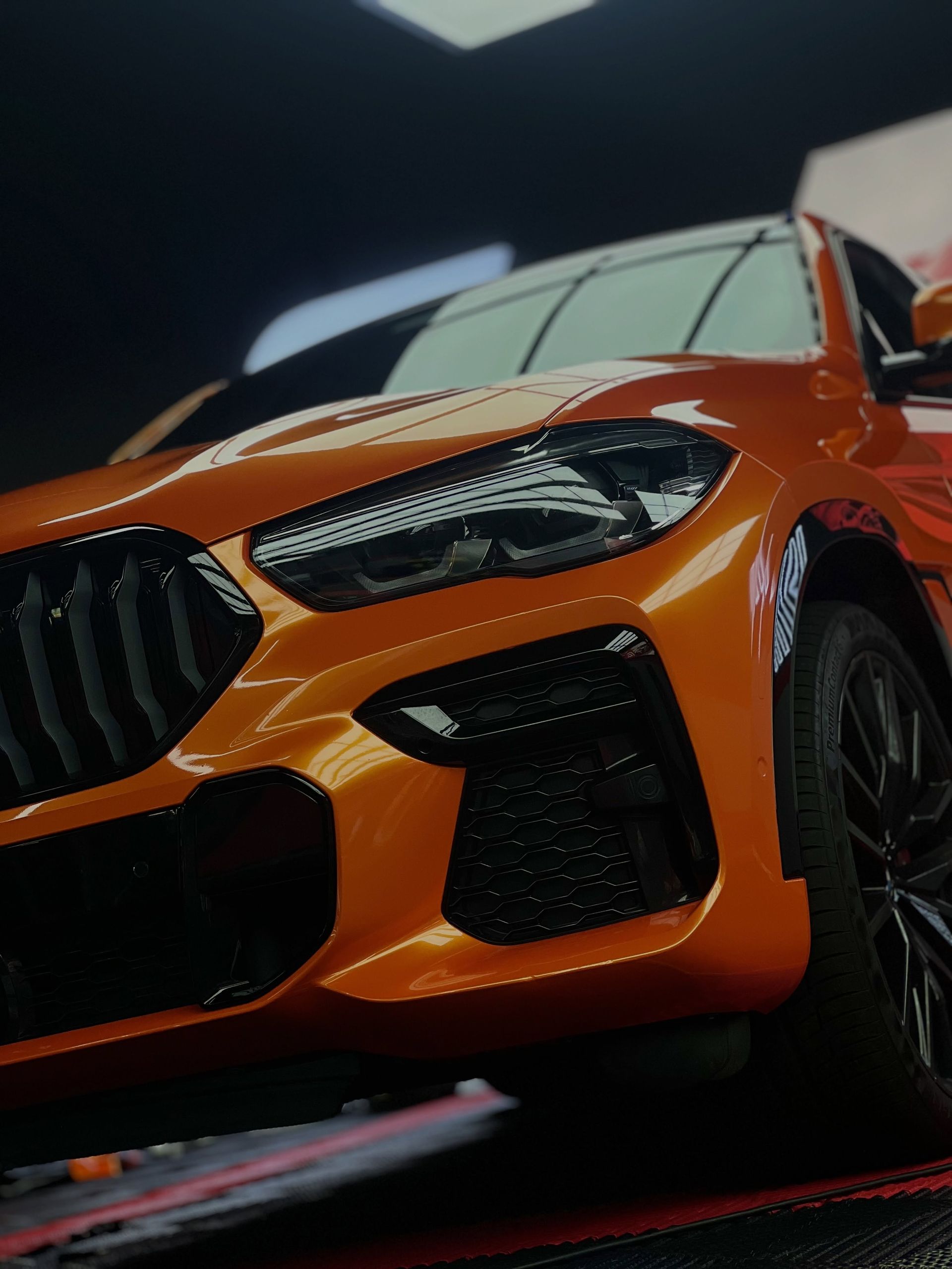 Orange sports car in a dark showroom, low-angle close-up of the front grille and headlights