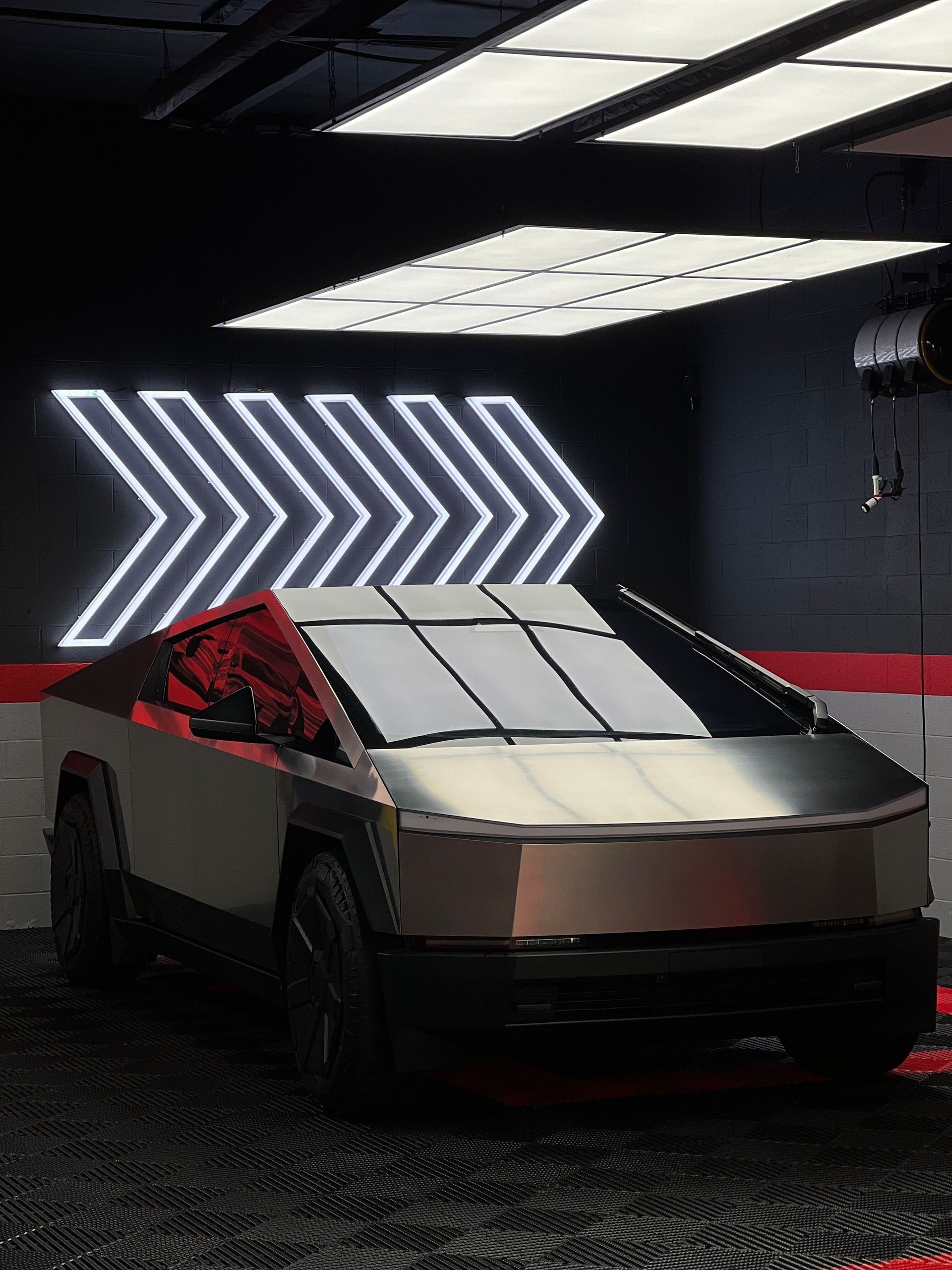 Silver angular Tesla Cybertruck in a dark showroom with neon arrow lights behind it