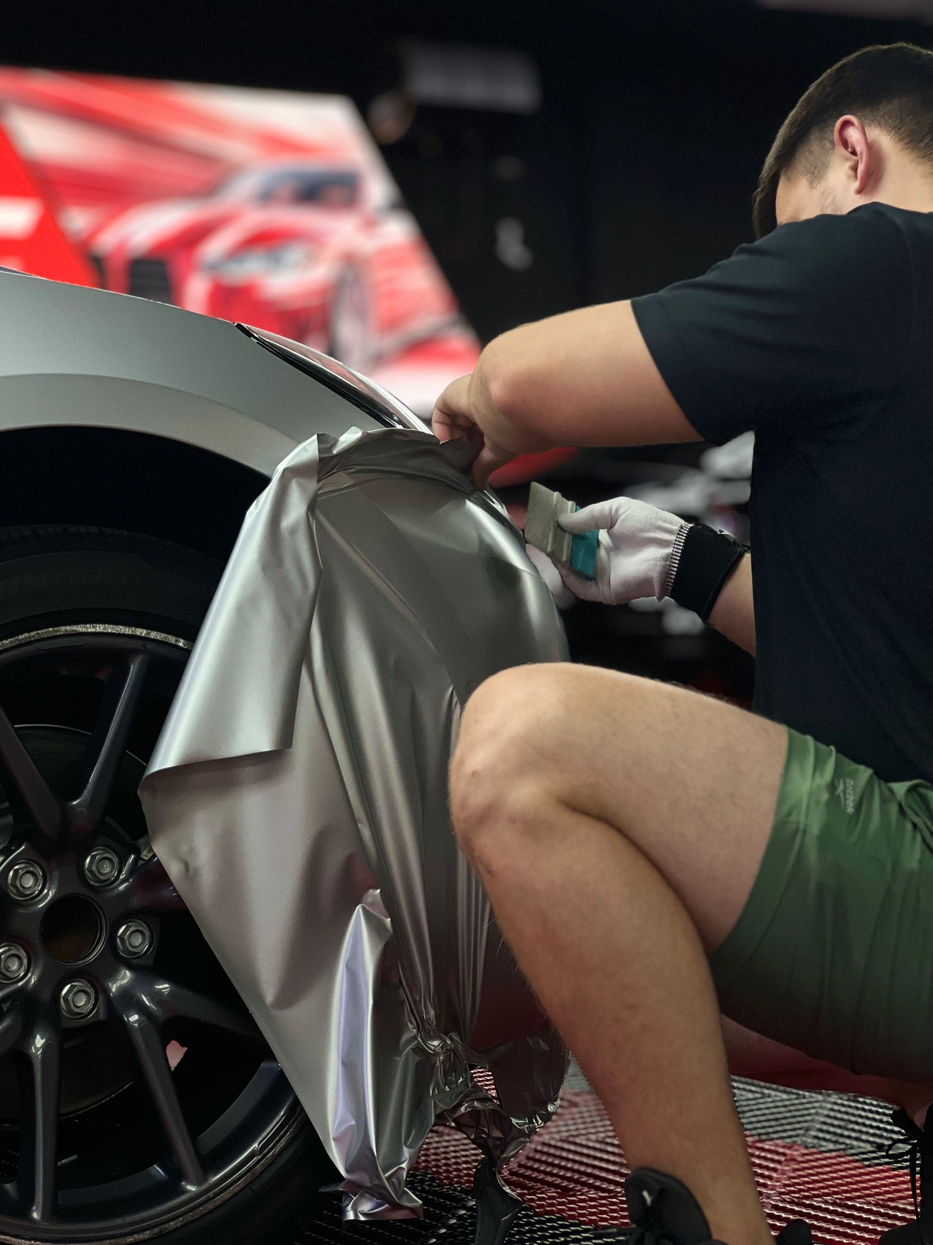 Person wrapping a car wheel in silver vinyl inside a workshop