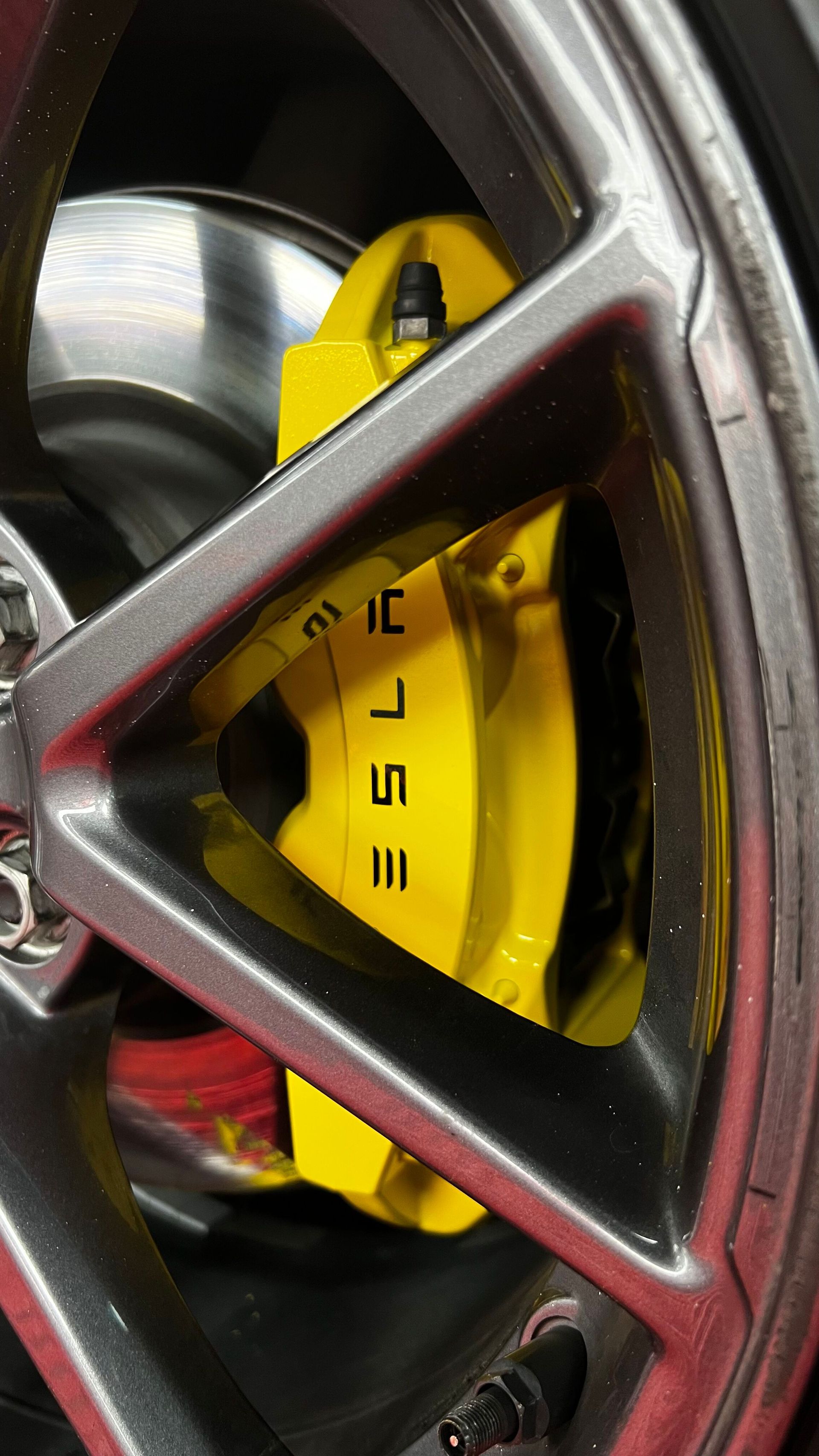 Close-up of a car wheel with a bright yellow brake caliper behind a silver rim