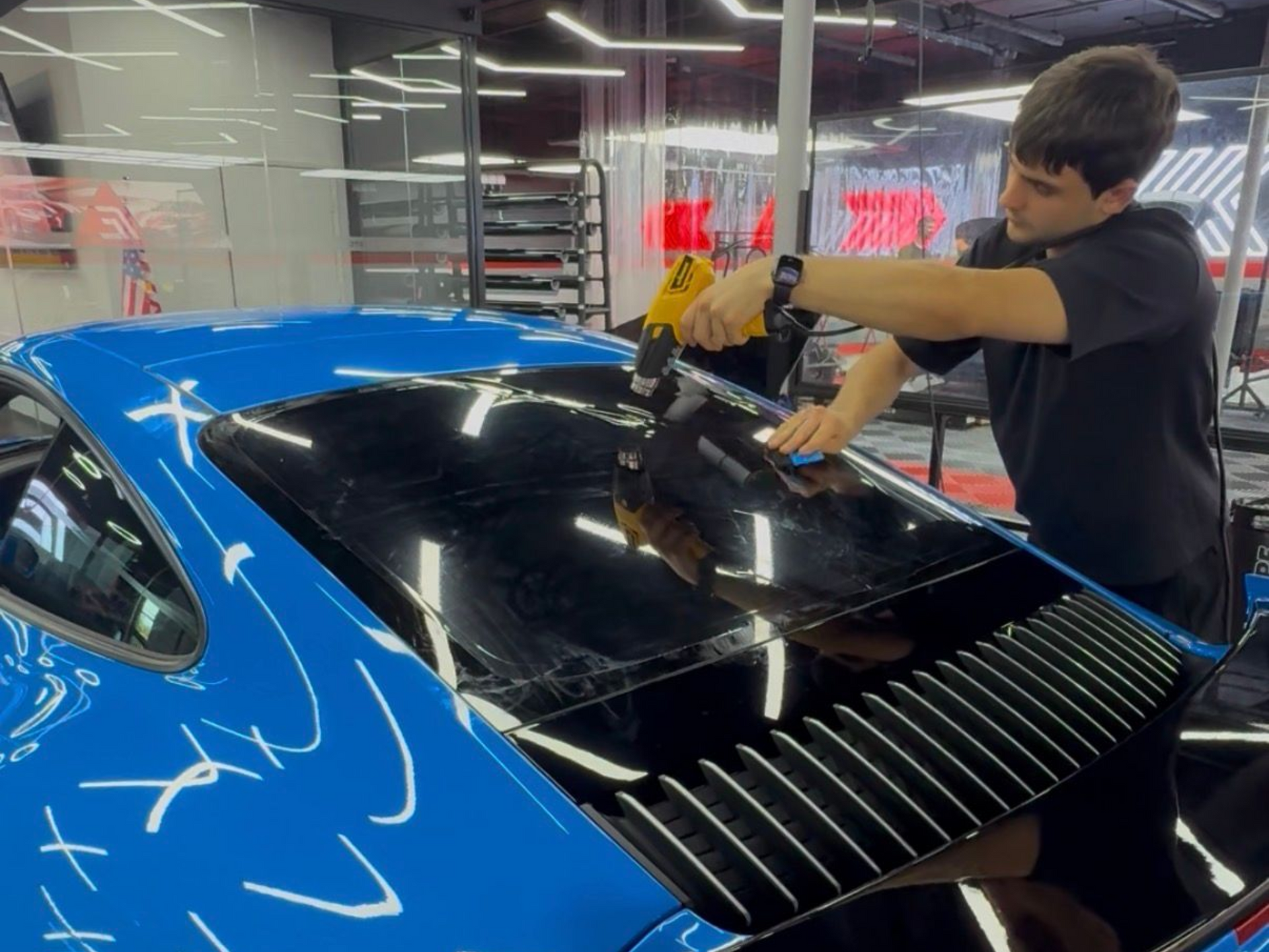 Car wrapped in black vinyl by gloved hands in a workshop