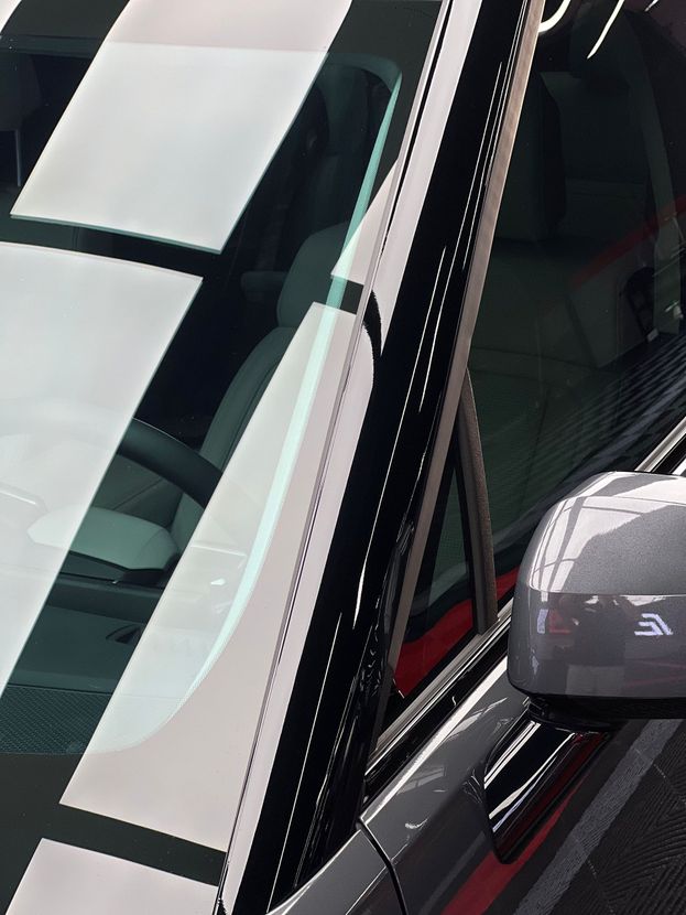 Close-up of a black car’s windshield, A-pillar, and side mirror with reflections on the glass.