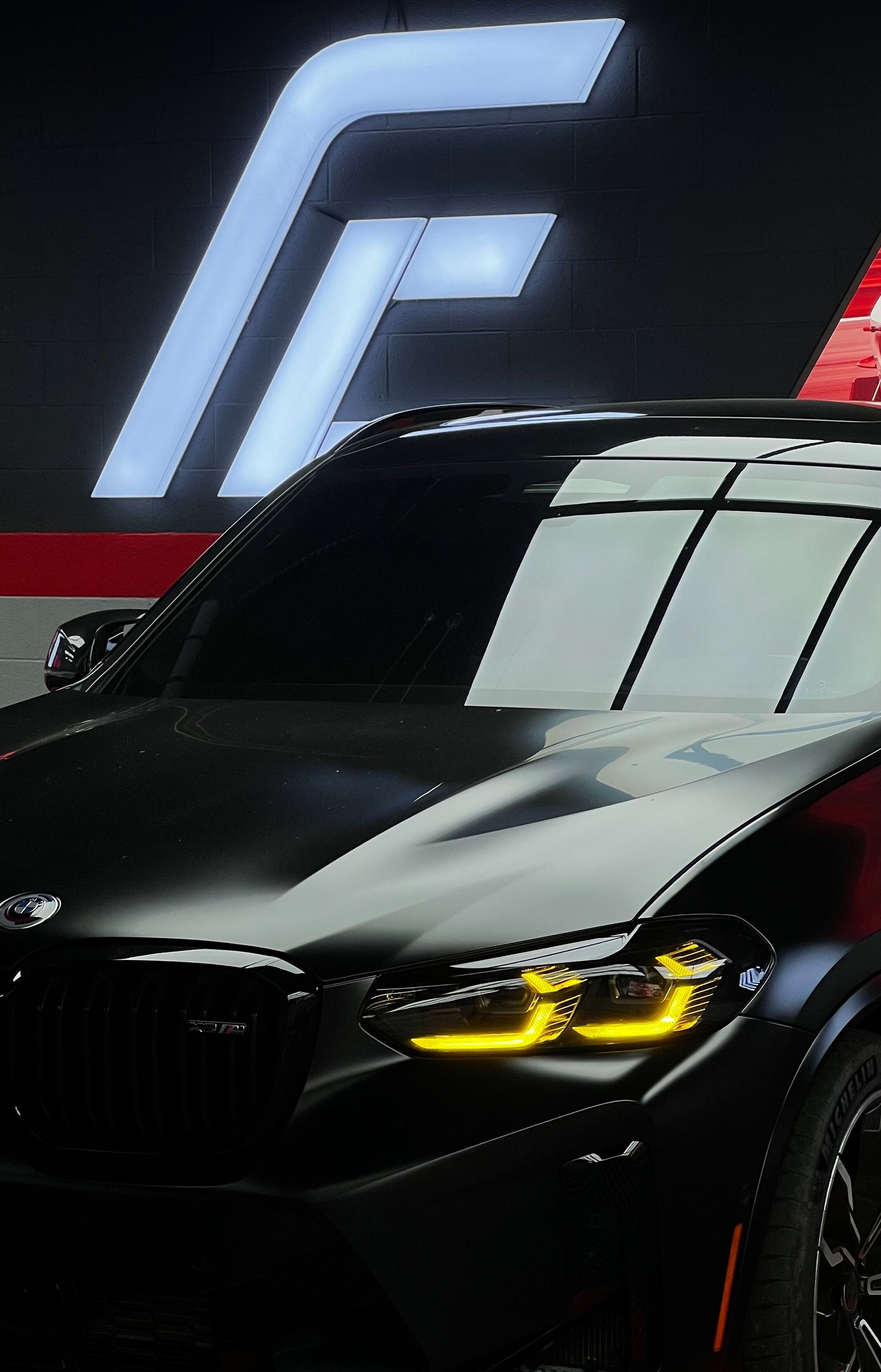 Black BMW with yellow headlights in front of a large illuminated E logo backdrop