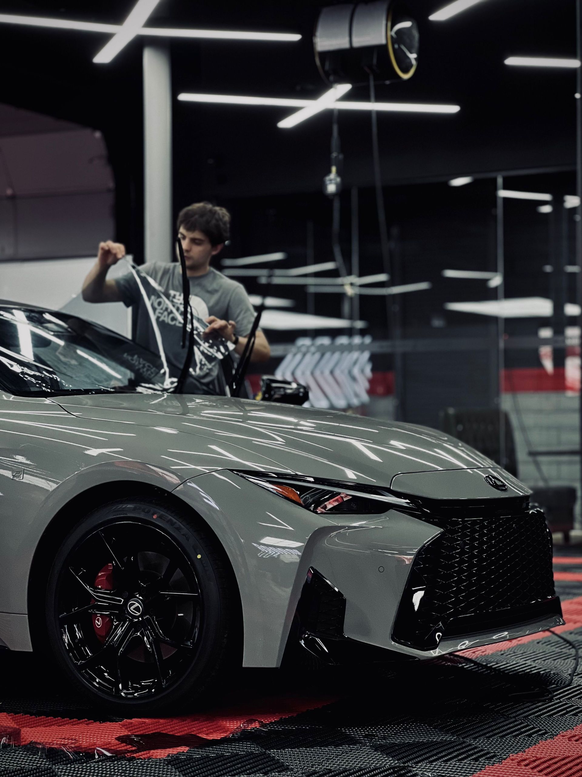 Person polishing a silver sports car in a showroom under bright overhead lights