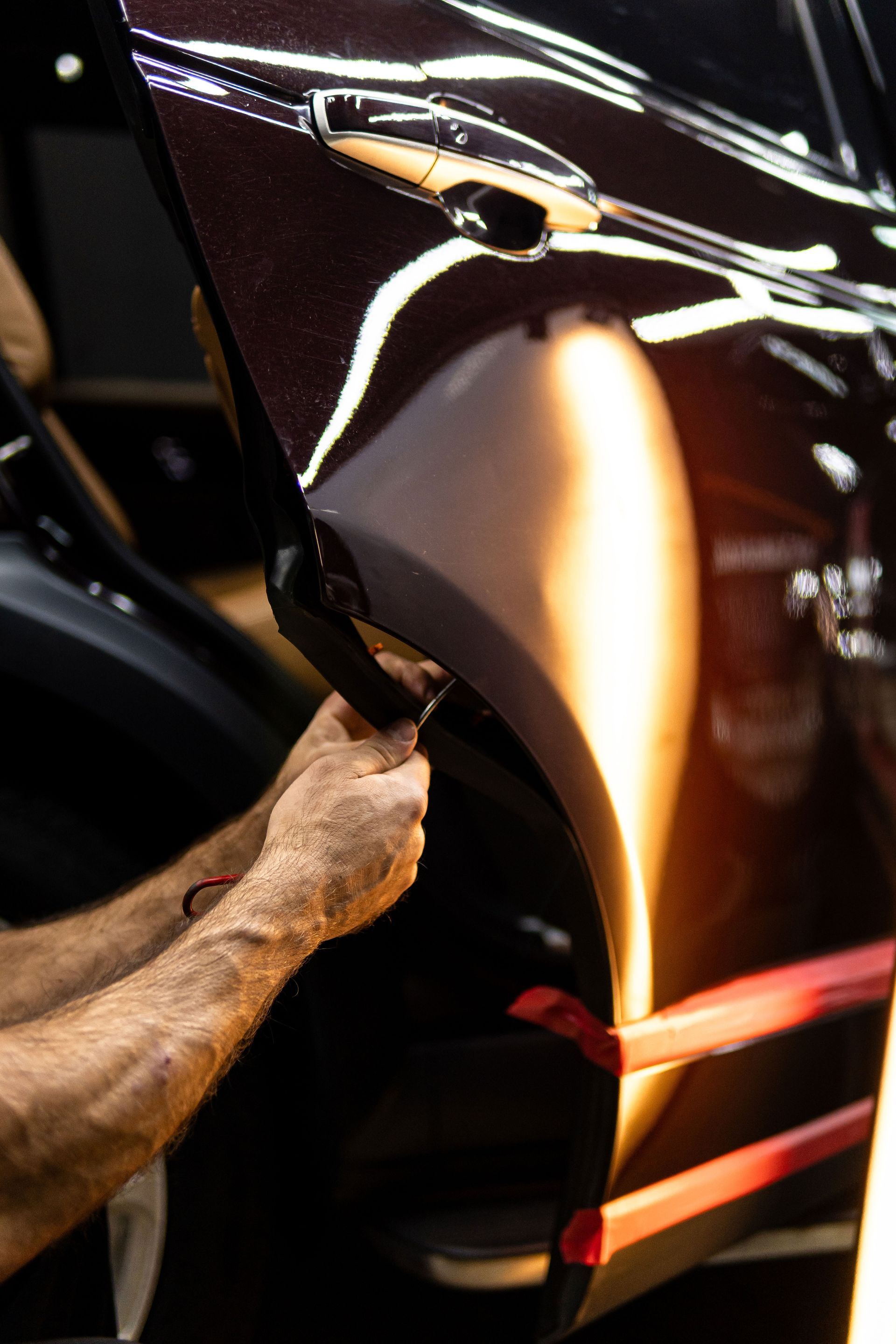 Close-up of a dark car’s dented door being repaired, with a hand using a heat gun