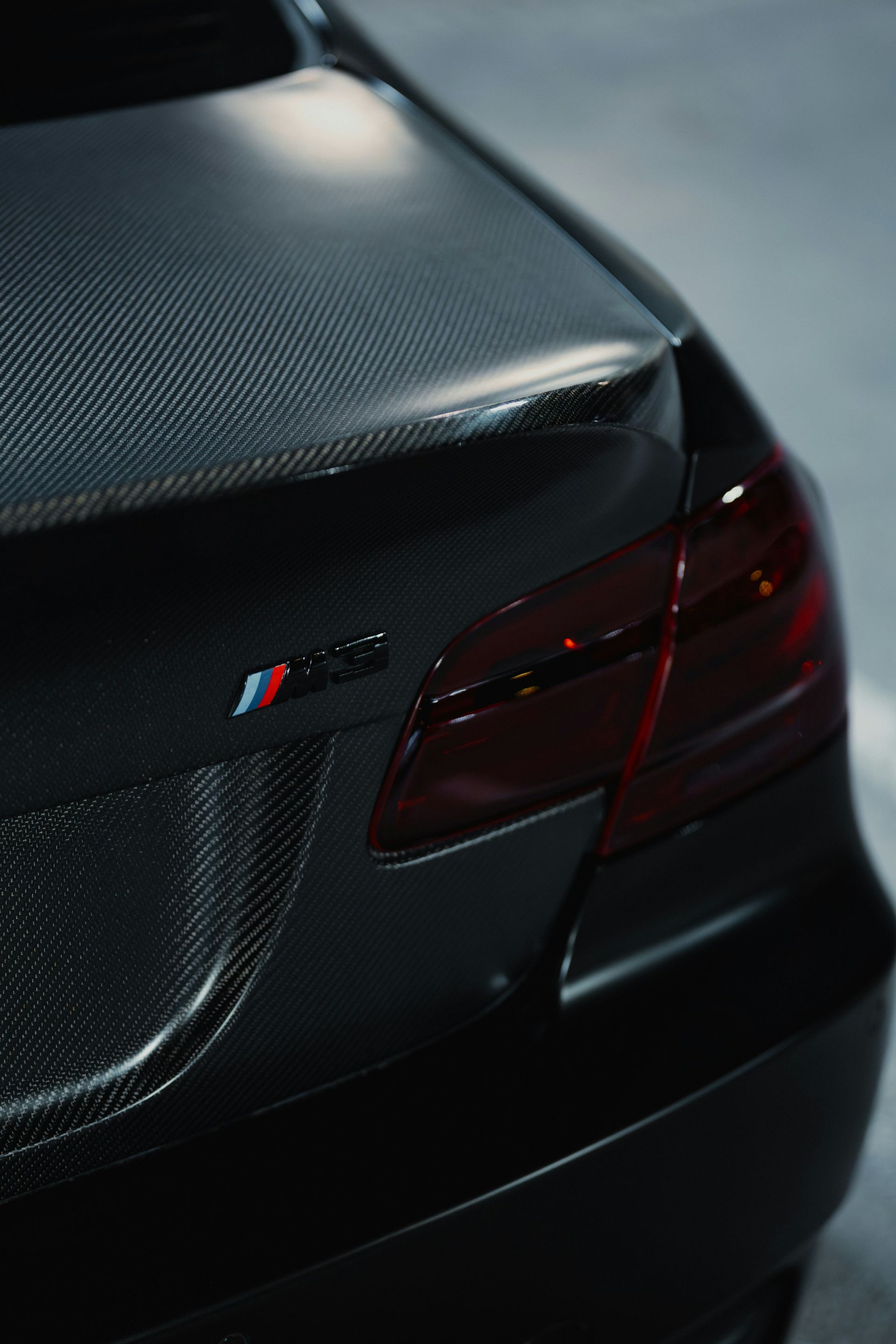 Close-up of a black BMW M car’s rear quarter panel and taillight on a dark background