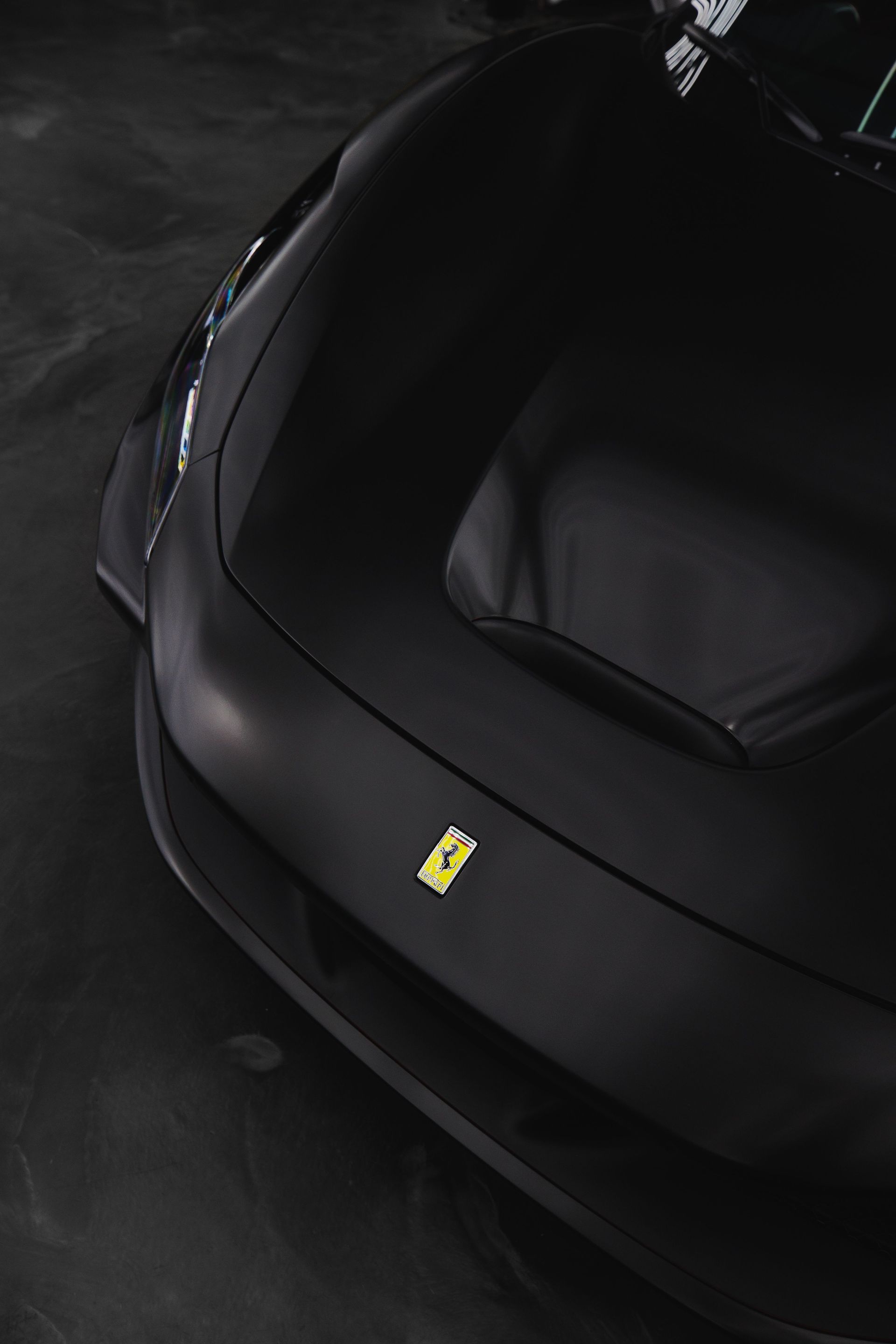 Black Ferrari sports car seen from above in a dark setting, with the yellow Ferrari logo on the hood