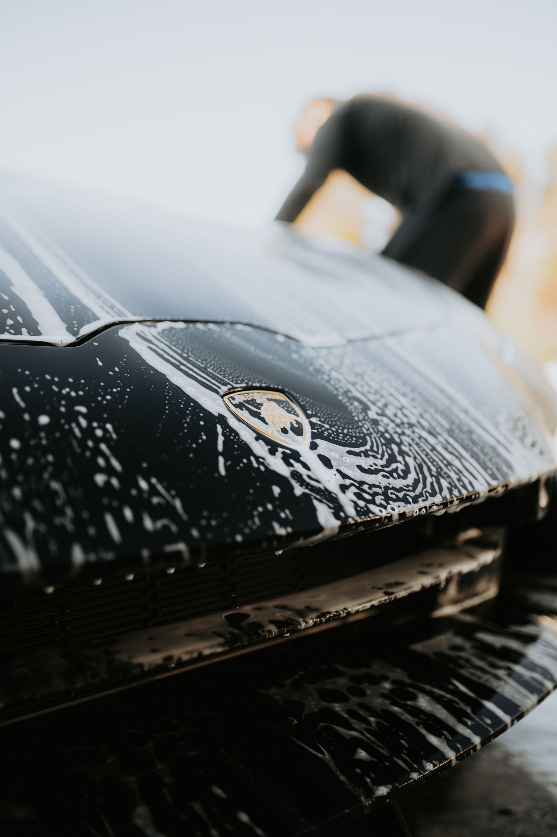 Person washing a black car hood with soapy water outdoors