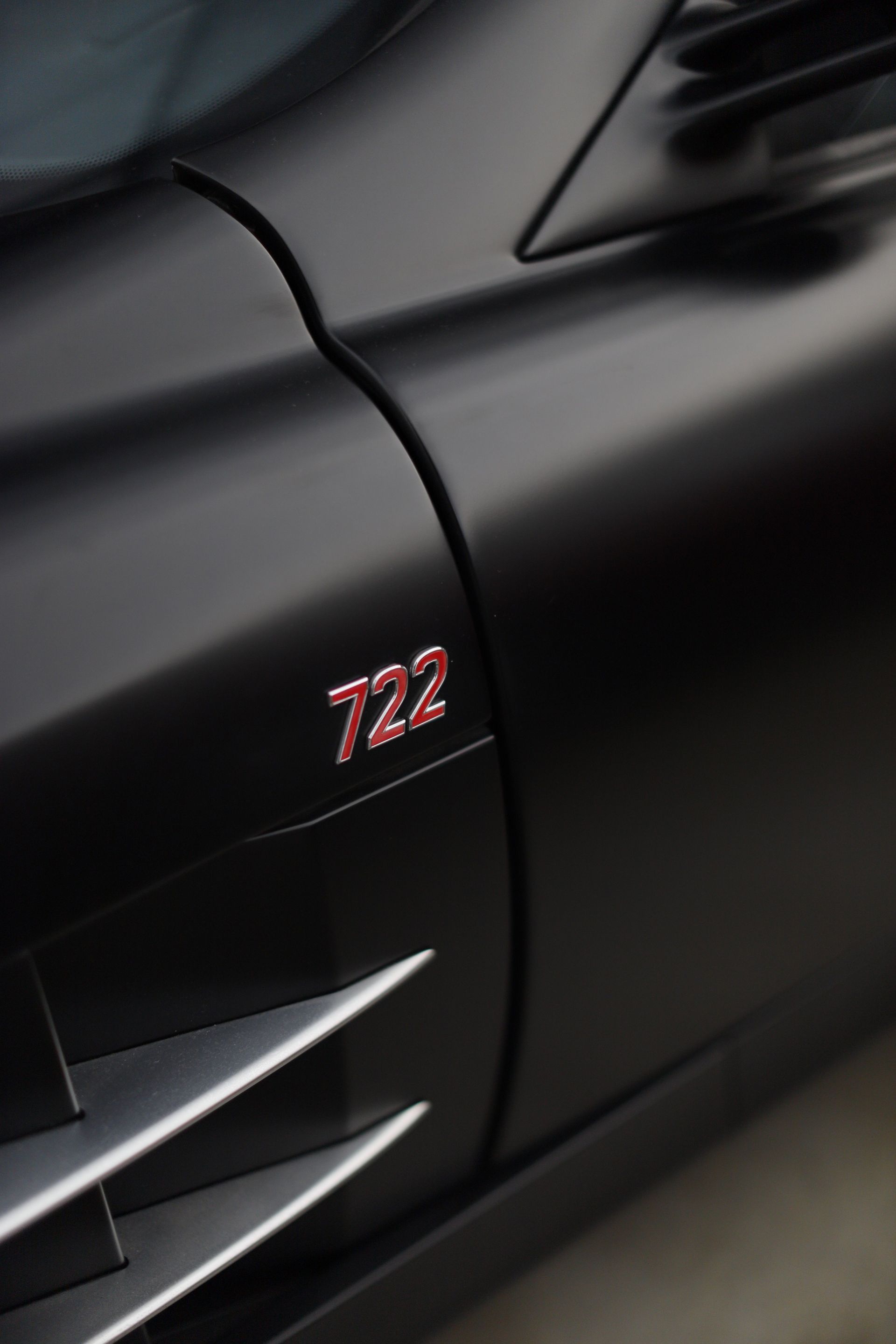 Close-up of a black sports car fender with red T22 badge and silver side vent