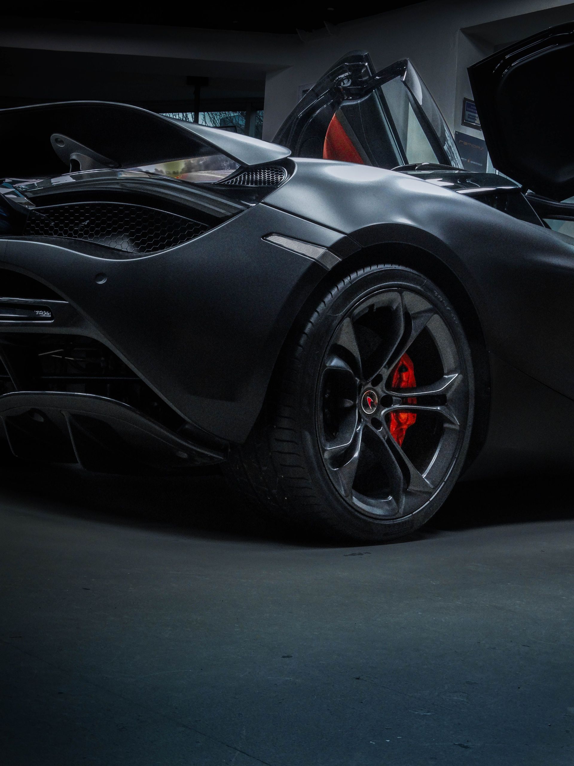 Black sports car with red brake calipers, shown in a dark studio with dramatic lighting.