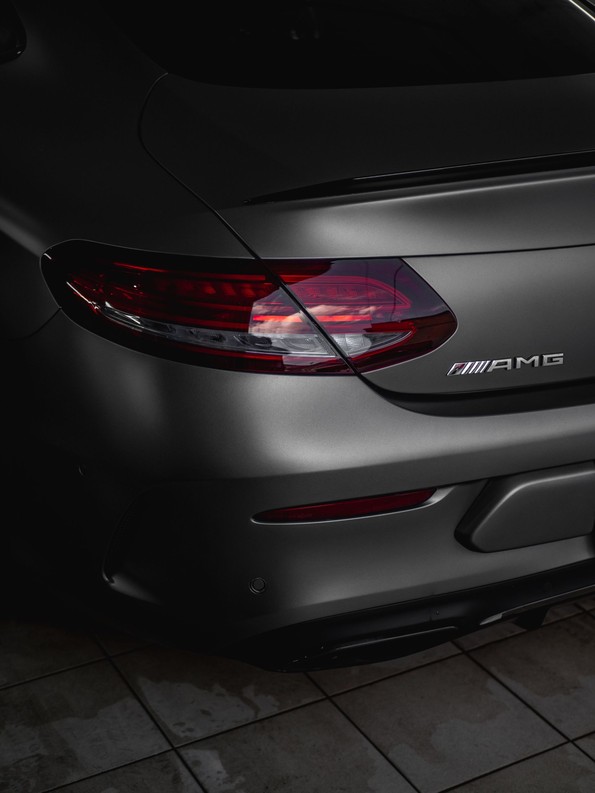 Rear view of a matte gray Mercedes-AMG sports car, showing the taillight and rear bumper at night.