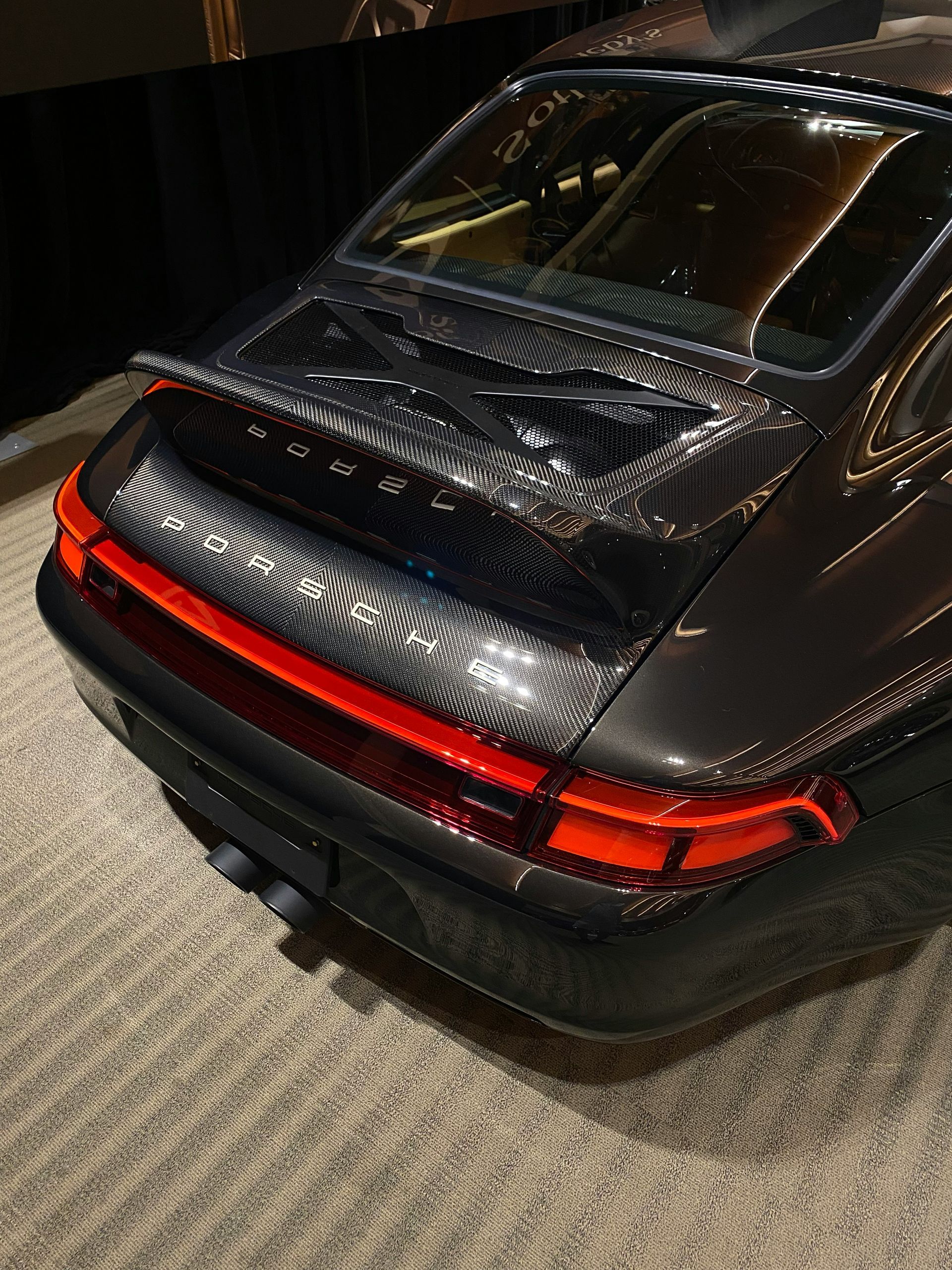 Rear view of a black sports car with a red light bar, parked indoors under display lighting