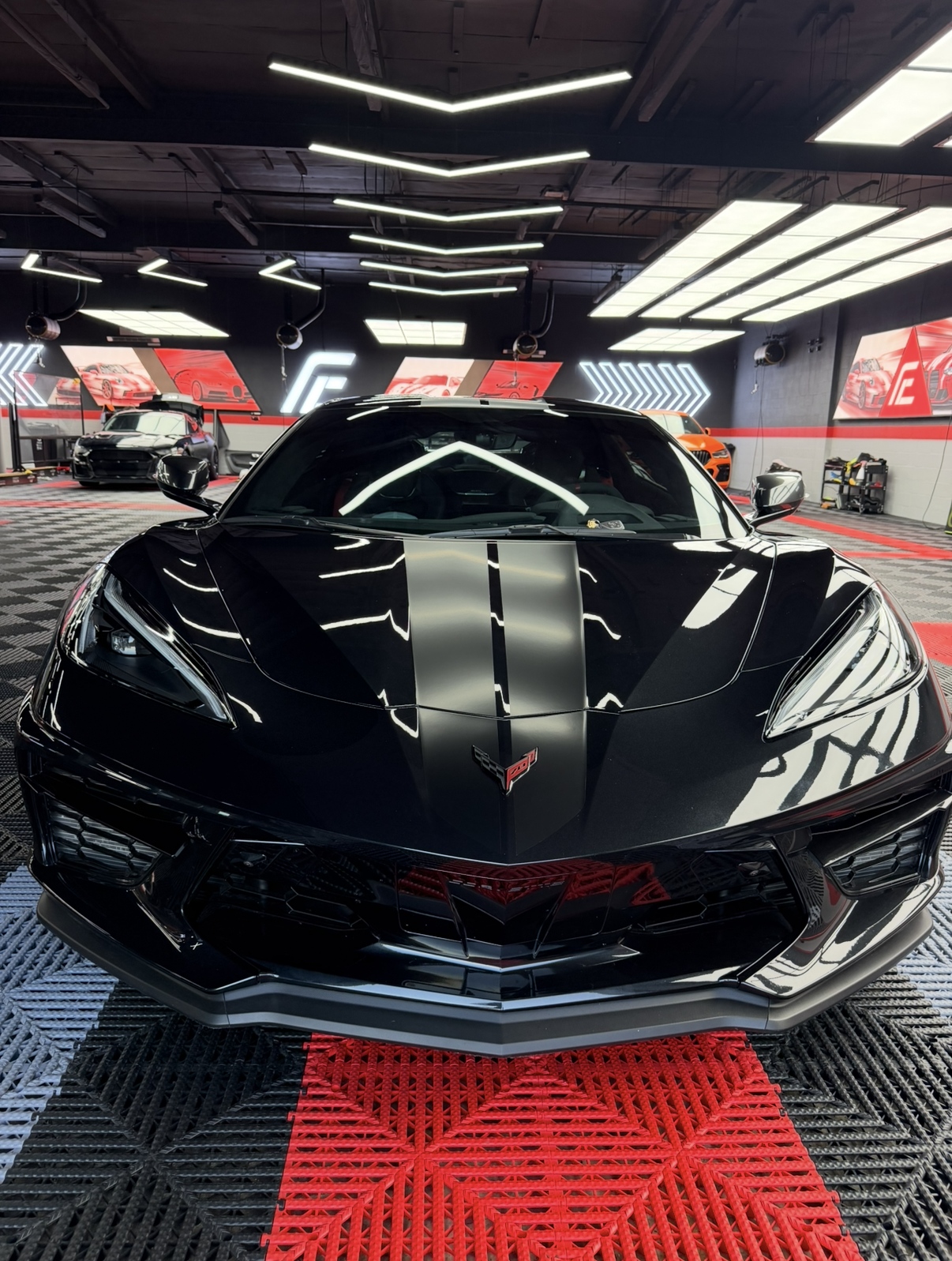 Black sports car with matte racing stripes displayed indoors under bright showroom lights.