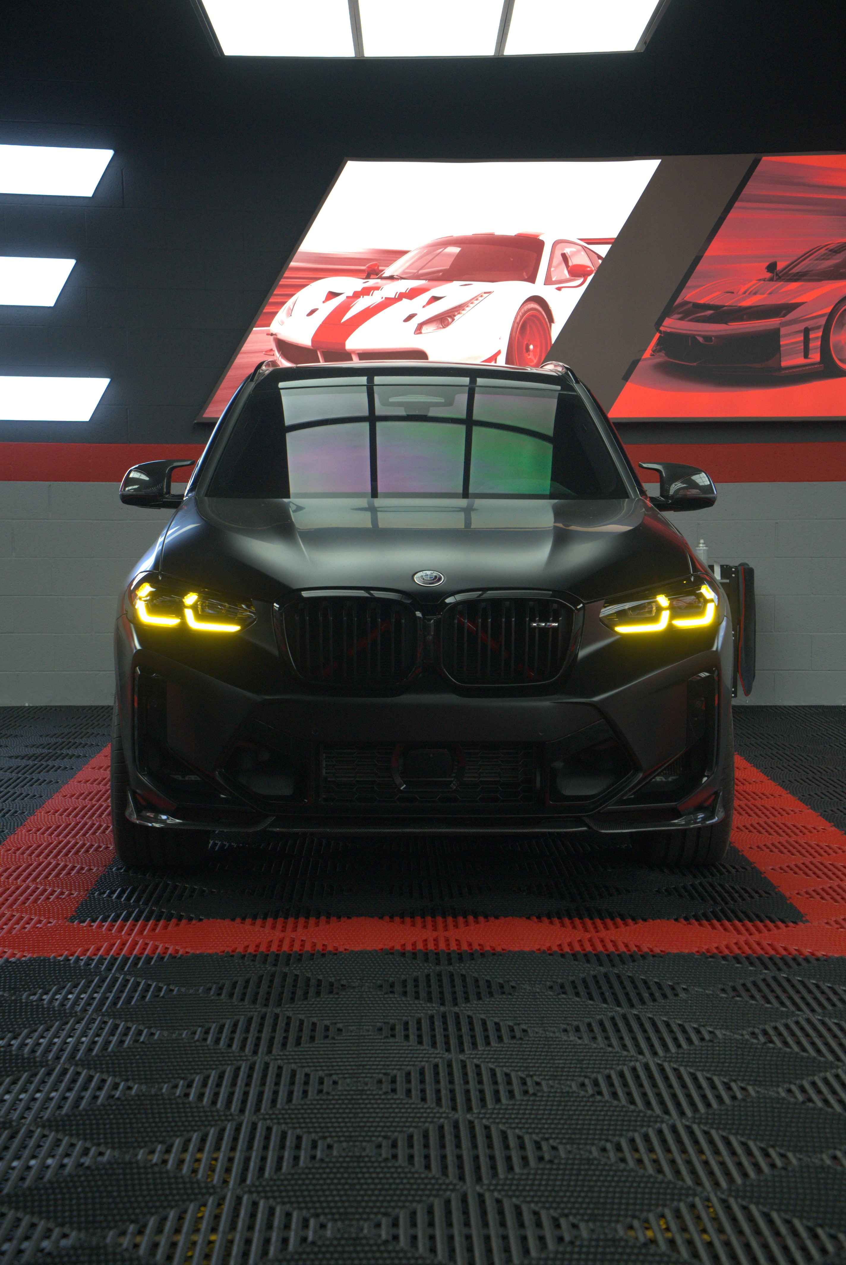 Close-up of a dark car front with pink LED headlights and a white fog light at night