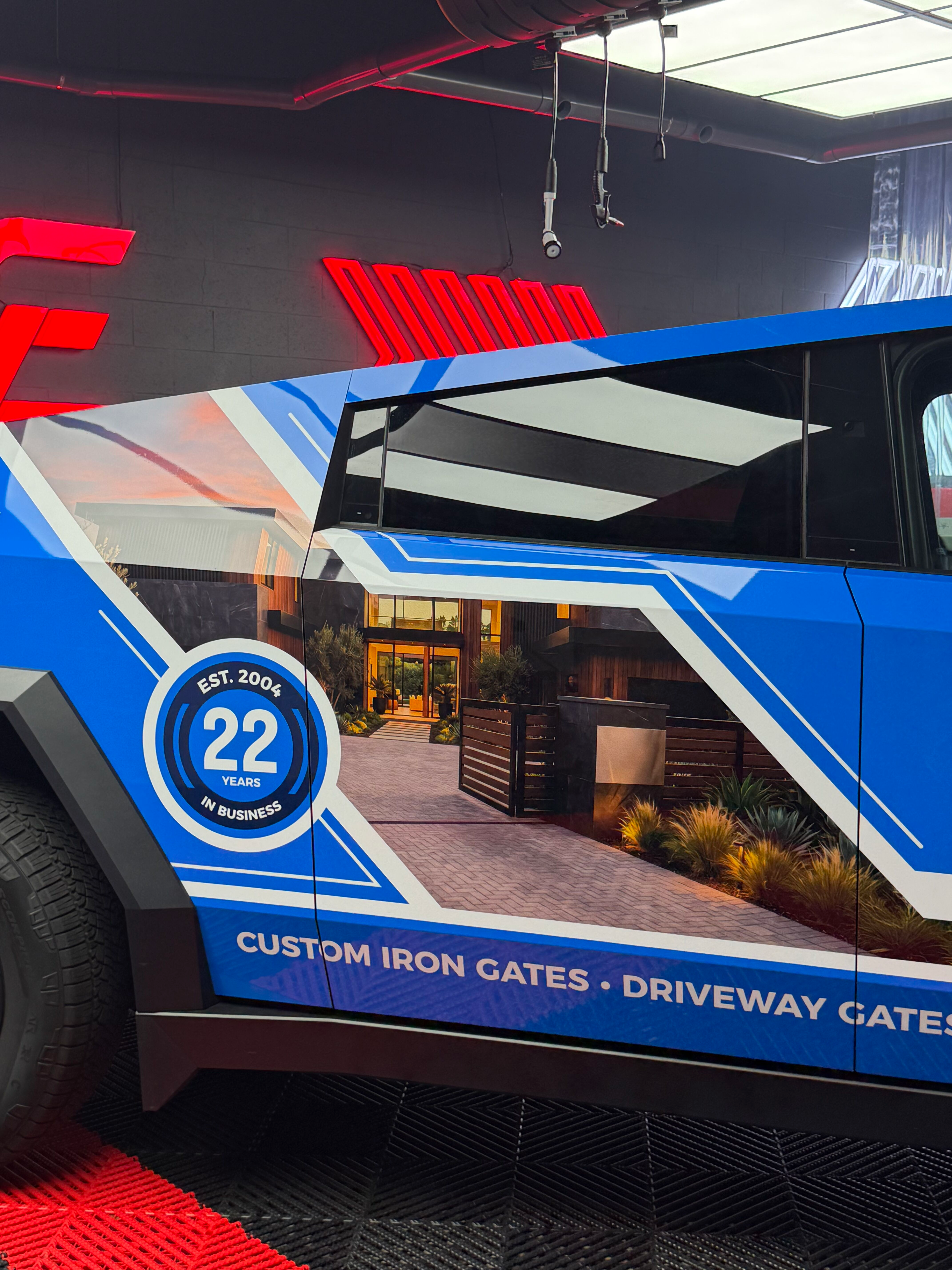 Blue custom gates van with red lights and storefront graphic; text reads “Custom Iron Gates - Driveway Gates.”