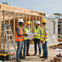 Construction workers in hard hats reviewing blueprints at a building site