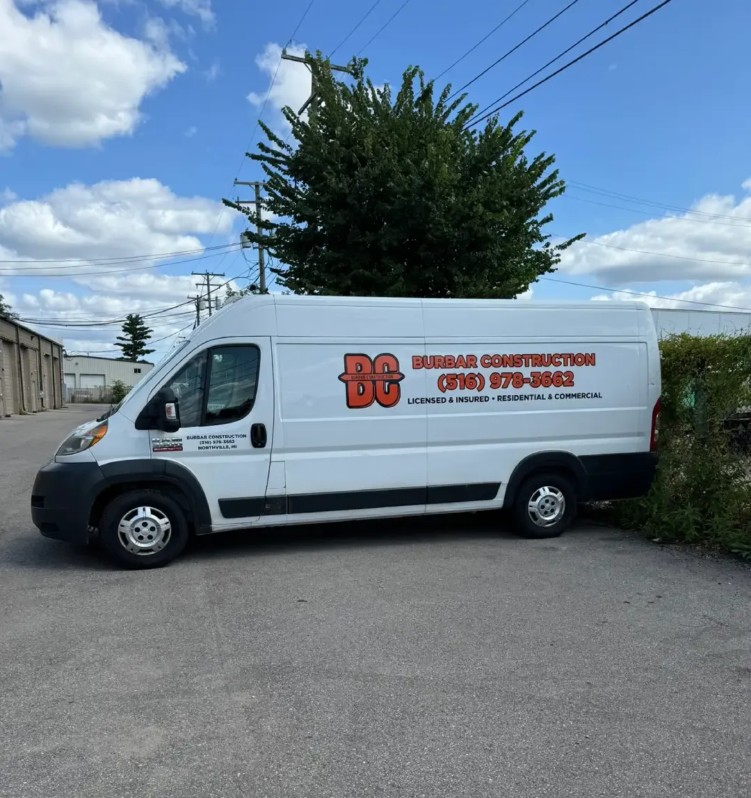 White cargo van with company logo and red lettering parked on a paved lot under a blue sky.