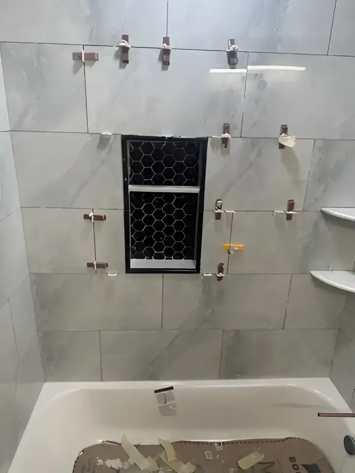 Tiled bathroom wall with a small frosted window and shower/tub fixtures being installed