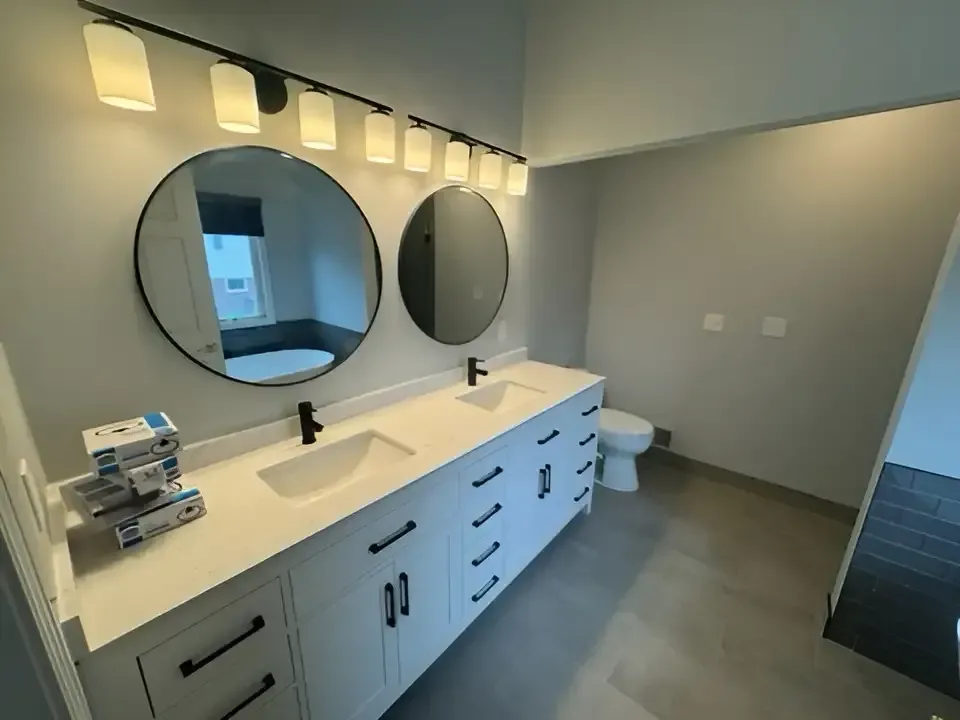 Modern bathroom with long vanity, round mirrors, sink, toilet, and soft wall lights