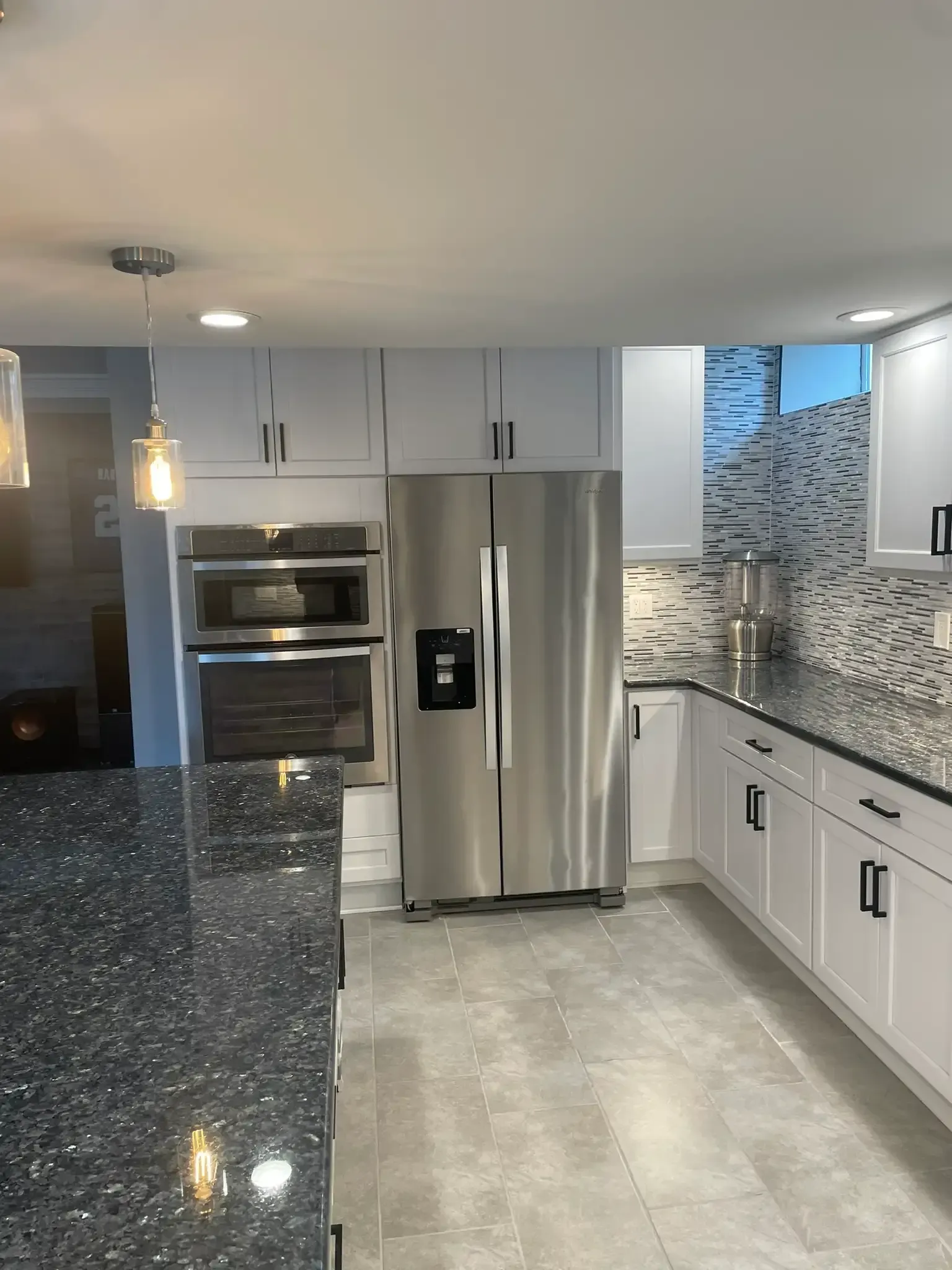 Modern kitchen with stainless steel appliances, gray cabinets, dark speckled island, and mosaic tile backsplash
