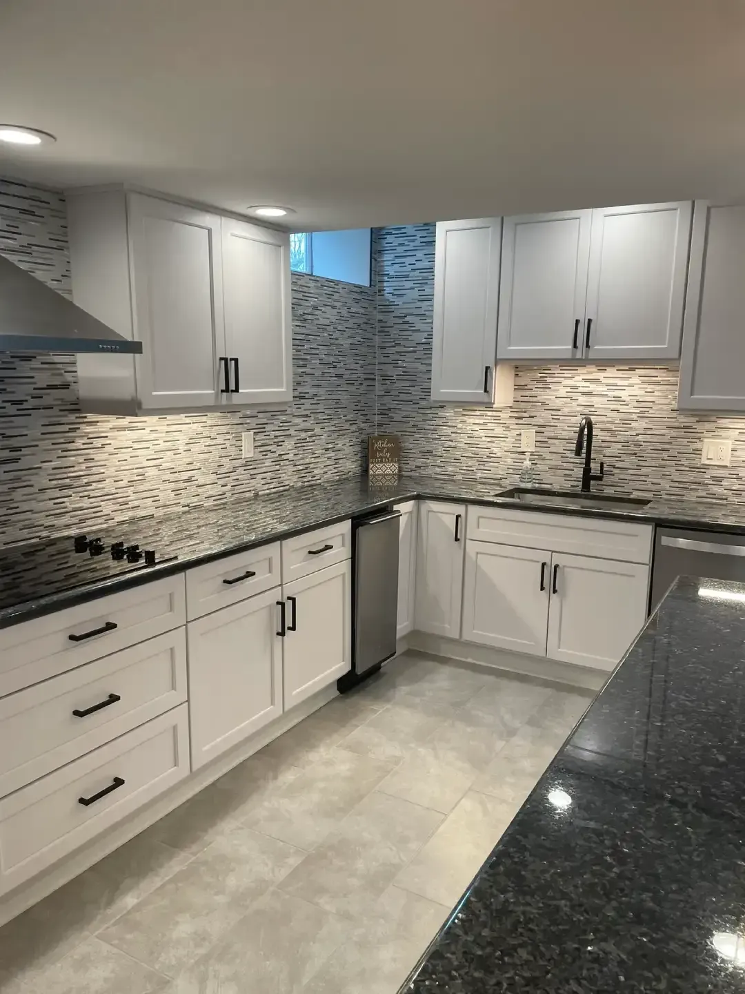 Modern white kitchen with mosaic tile backsplash, dark countertops, and light tile floor