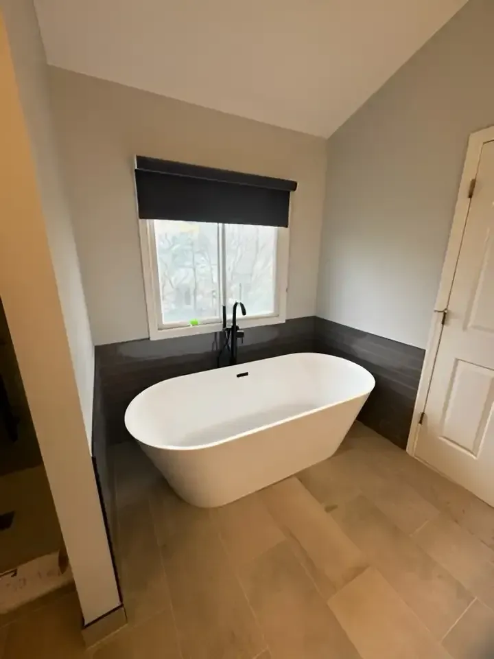 Modern bathroom with a freestanding white tub beneath a window and dark wood paneling