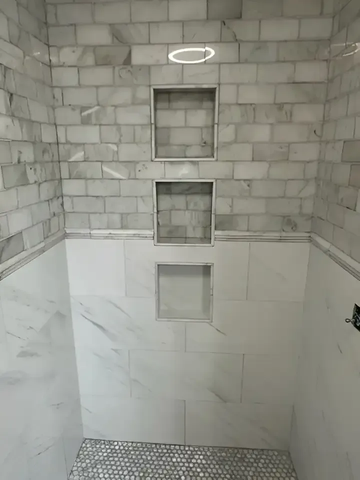 Tiled bathroom shower niche with three recessed shelves and unfinished gray block walls