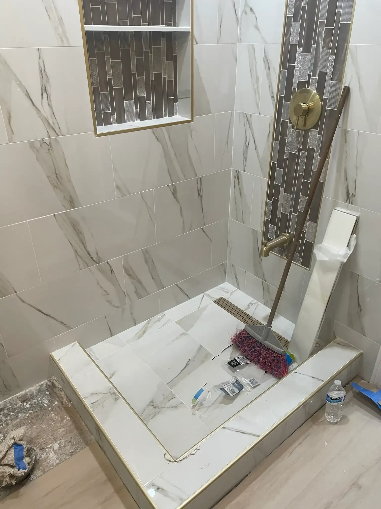 Tiled bathroom shower with white tray, glass panel, and cleaning tools on the floor.