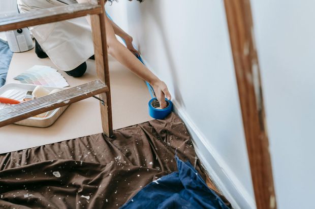 Person painting a wall, using blue painter’s tape and a drop cloth to protect the floor