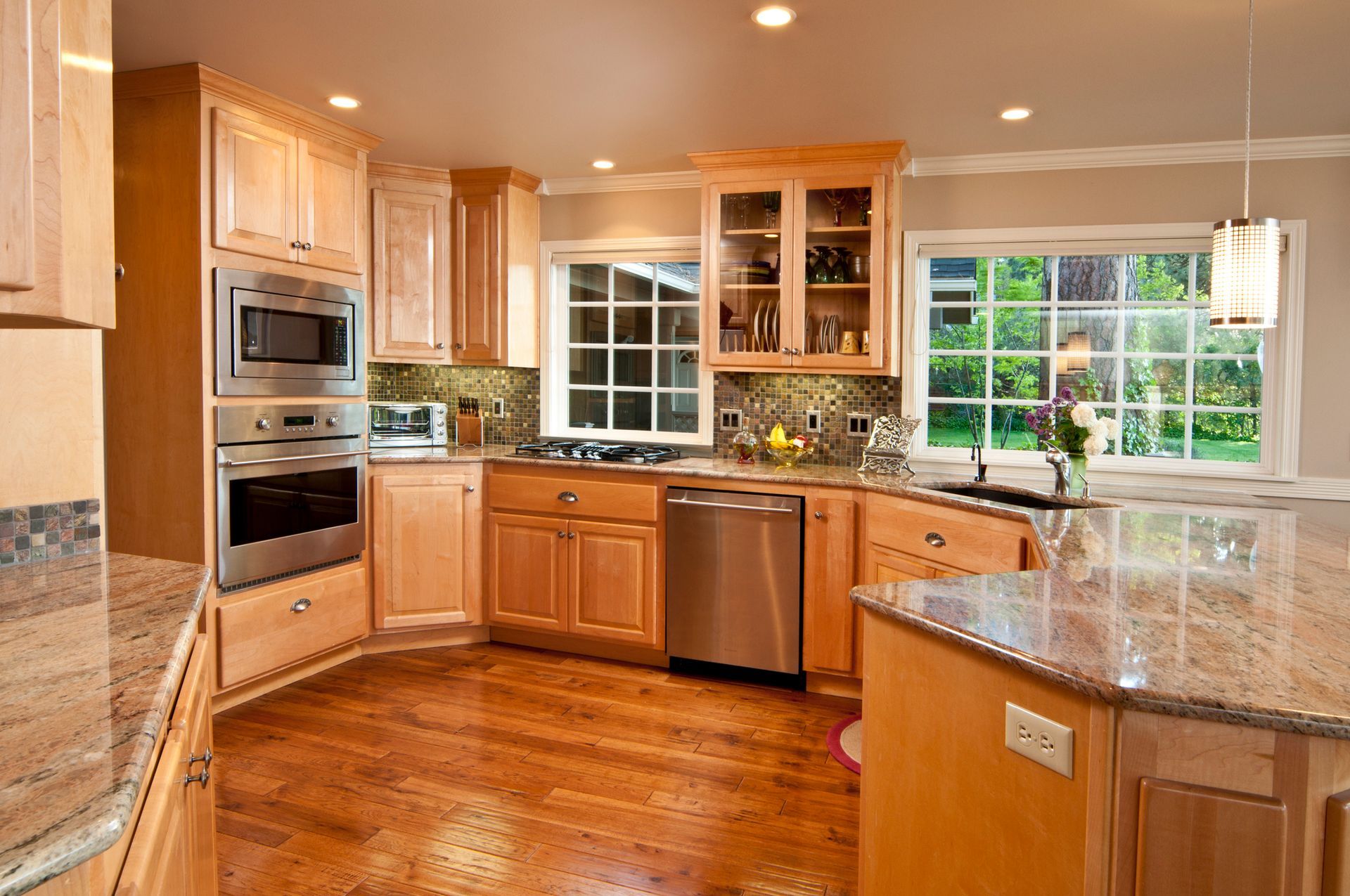 A kitchen with wooden cabinets , granite counter tops , stainless steel appliances and a large window.