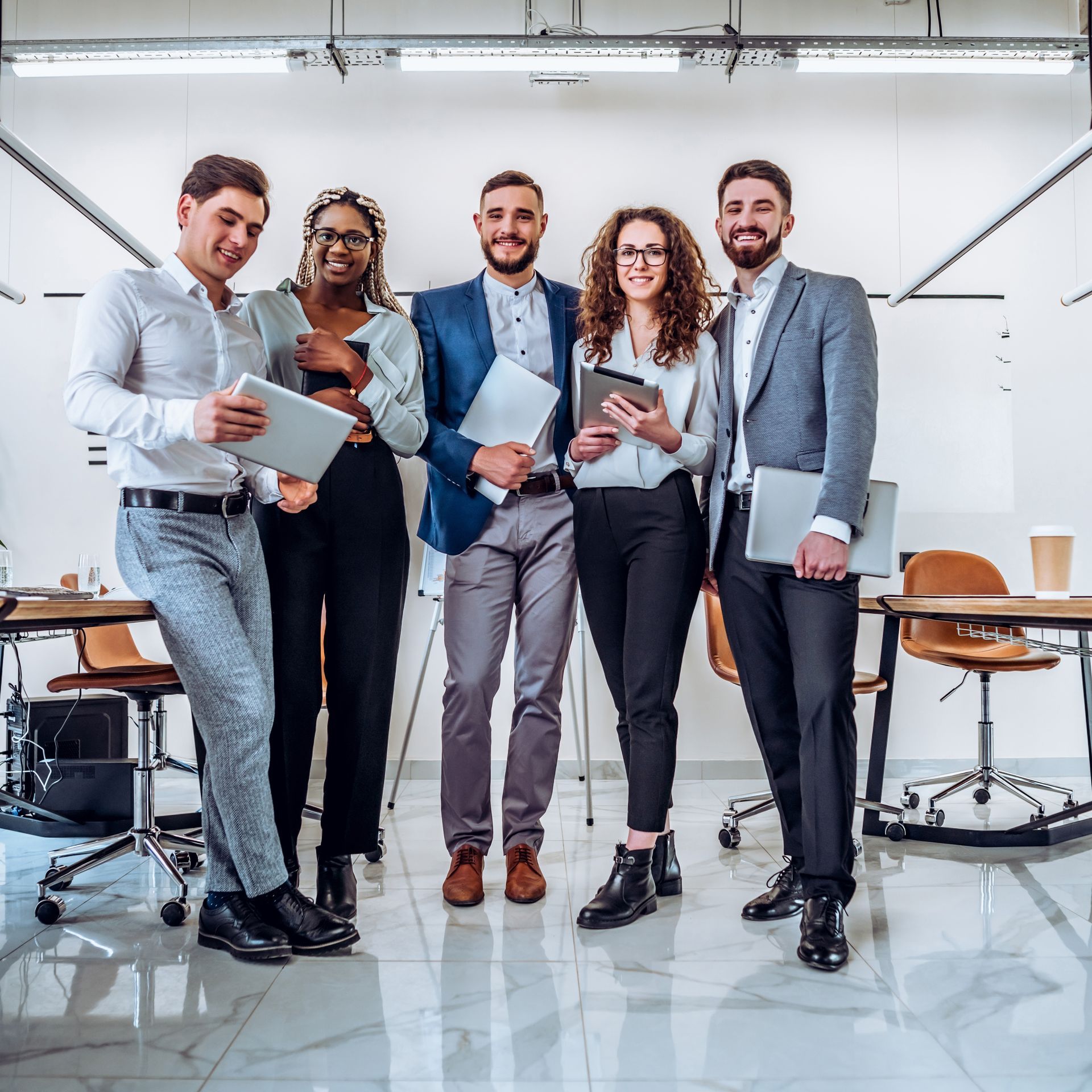 Group of people standing in an office, holding tablets and smiling.