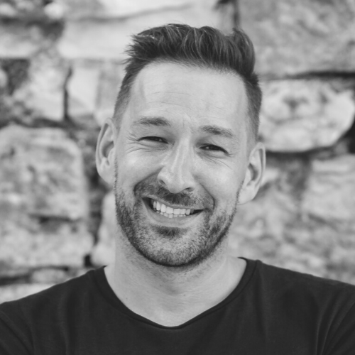 Auf einem Schwarzweißfoto lächelt ein Mann mit Bart.