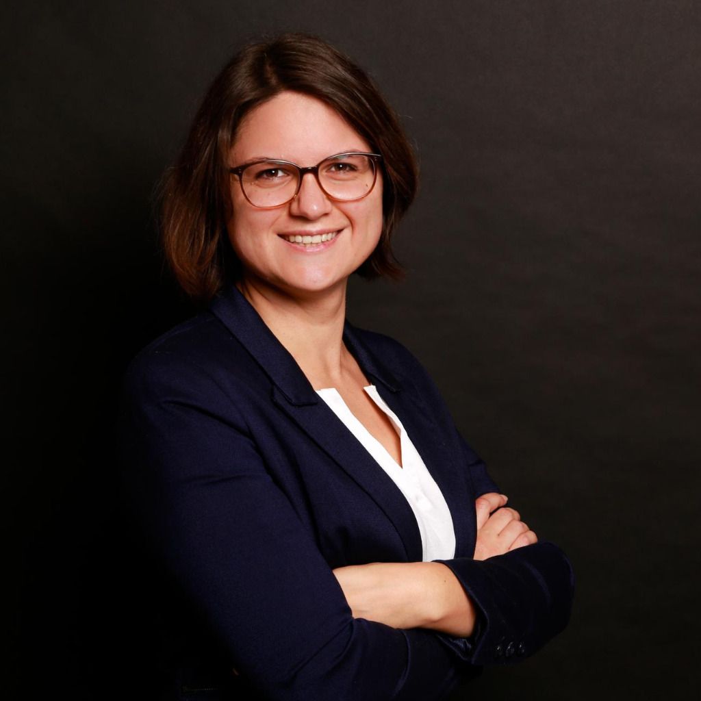 Eine Frau mit Brille und blauer Jacke lächelt und verschränkt die Arme.