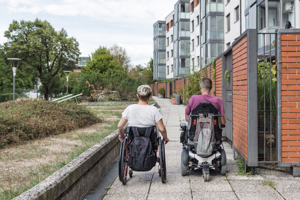 two people in wheelchairs are walking down a sidewalk.