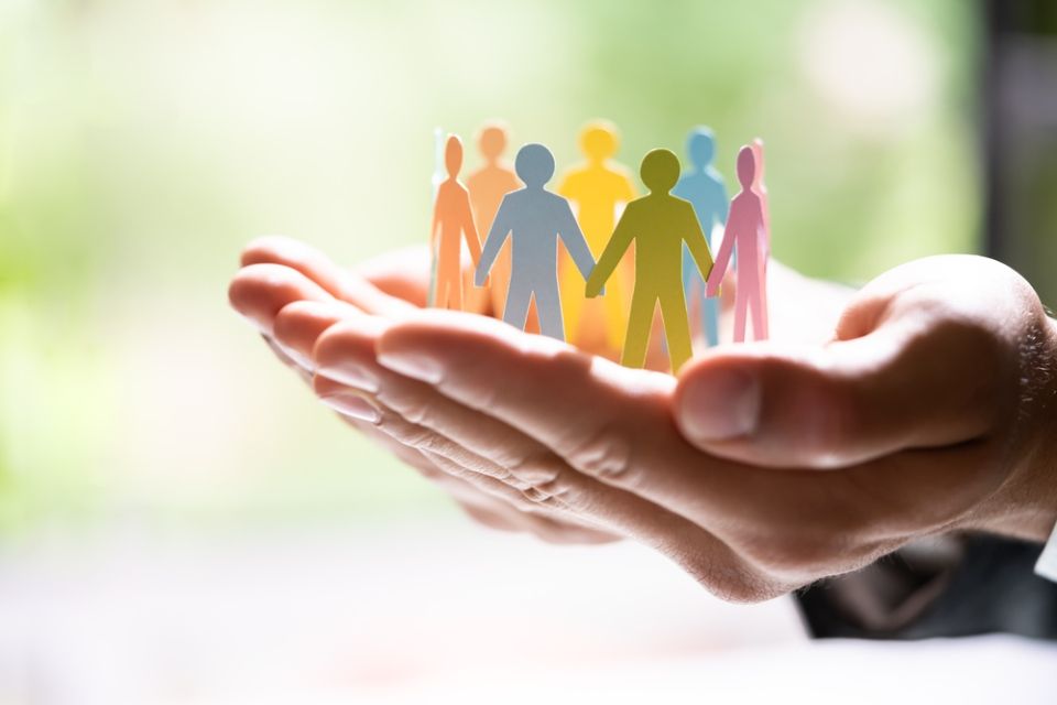 A person is holding a group of paper people in their hands.