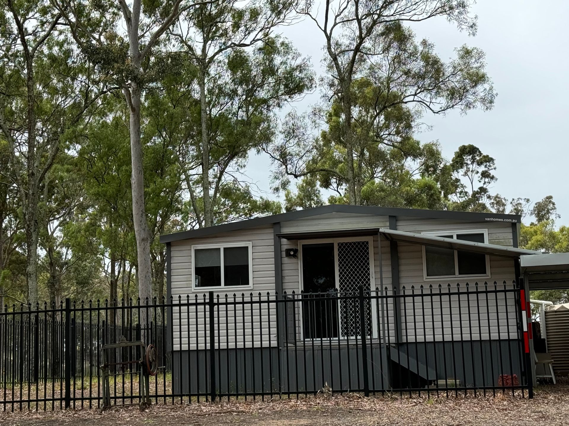 A small house with a fence around it and trees in the background.