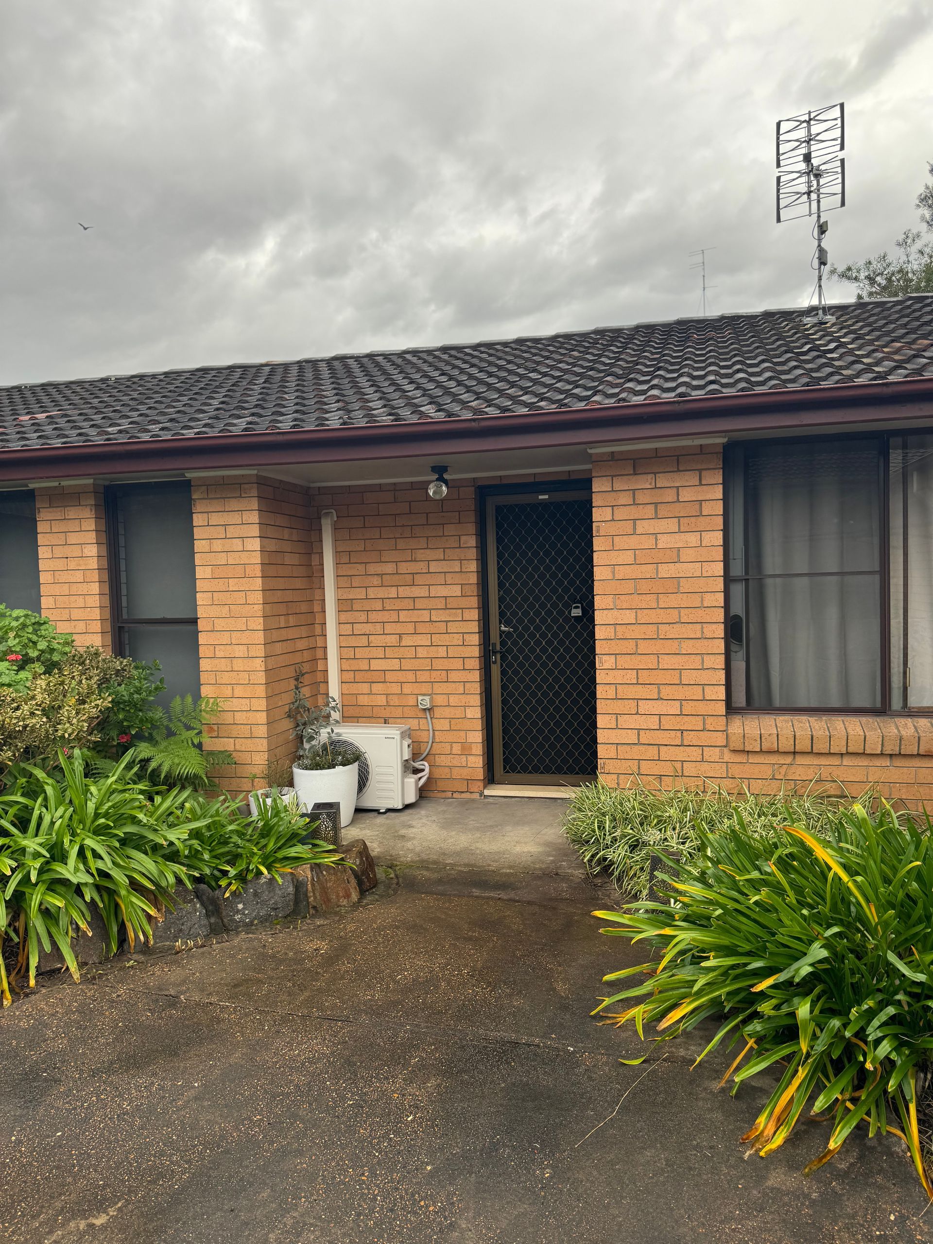 A small brick house with a roof and a few plants in front of it.